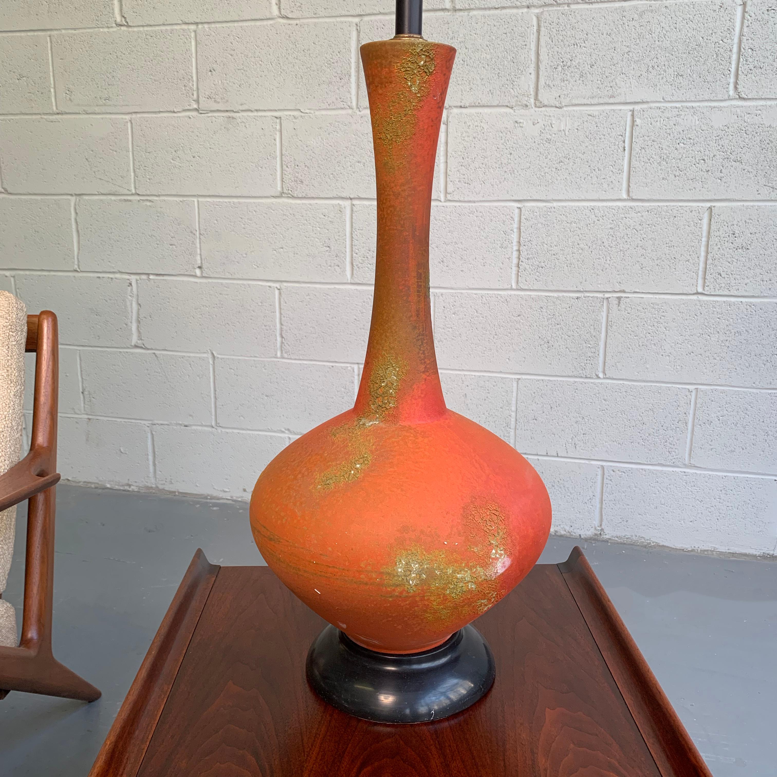 Large, Mid-Century Modern, art pottery, table lamp features a Brutalist, ceramic, lava textured orange orb base with elongated neck and spun black metal base and neck.