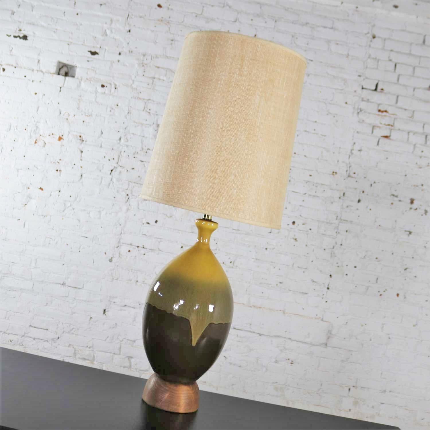 Handsome large Mid-Century Modern ceramic table lamp with a brown and golden yellow drip glaze on a wood base. It wears its original hard lined linen look tall drum shade. Both are in wonderful condition. It has been rewired and given a new socket.