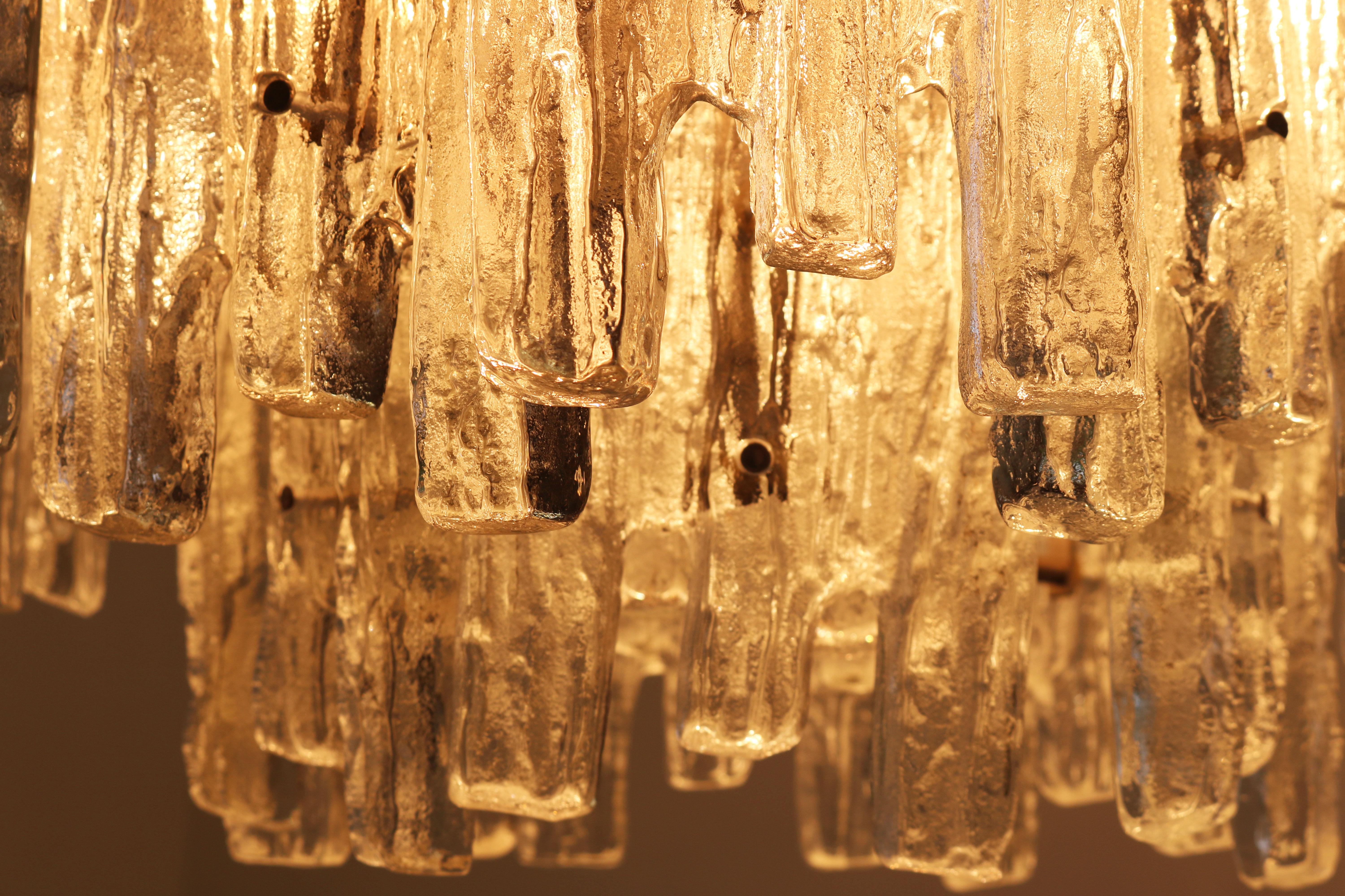 Intemporel et magnifique ! Ce J.T. de 18 lumières Lustre design Kalmar, fabriqué en 1960 en Autriche par Kalmar. Cette pièce exquise présente un cadre chromé élégant orné de 21 grandes pièces de verre glacé hypnotisantes, créant un affichage