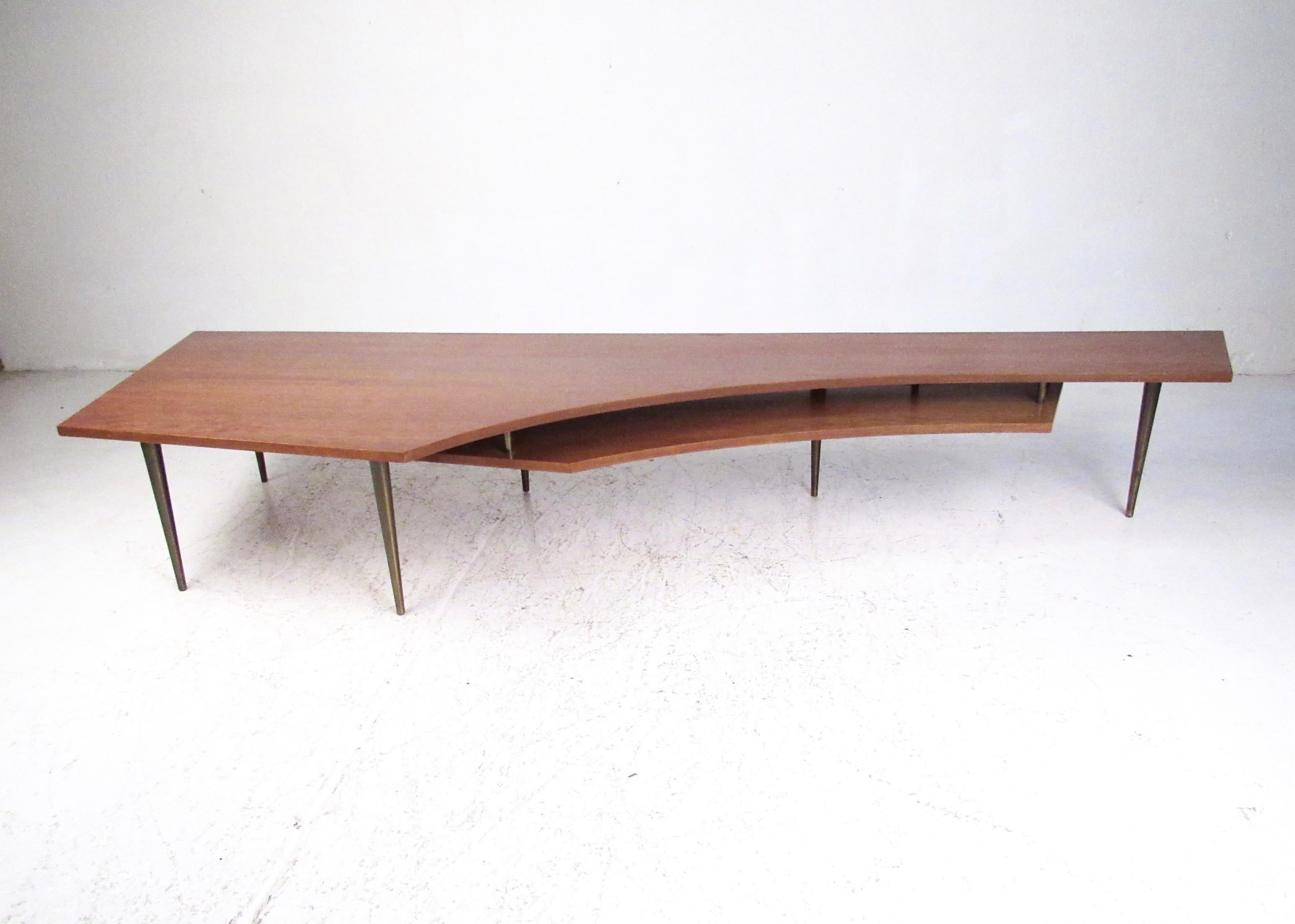 This large-scale two-tier coffee table features distinctive midcentury design, tapered bronze finish legs, and geometrically shaped cut away tabletop. The unique shape makes this an ideal cocktail table for home or business sofa seating areas,