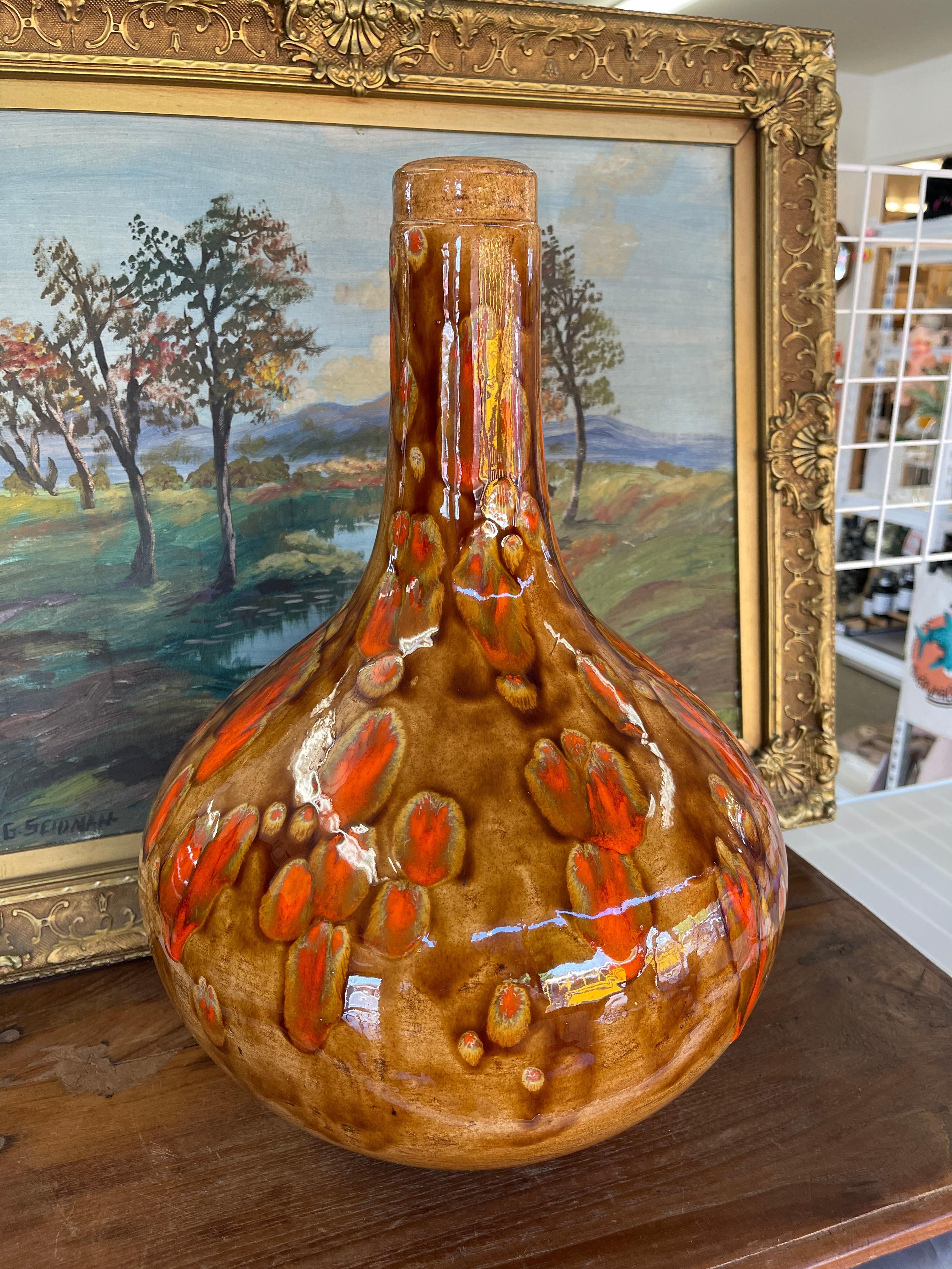 This striking mid-century modern pottery vase, that could have formerly been a lamp base, features a dramatic bottle form with a tall neck and wide, bulbous body. The surface is finished in a richly glazed palette of warm brown and ochre tones,