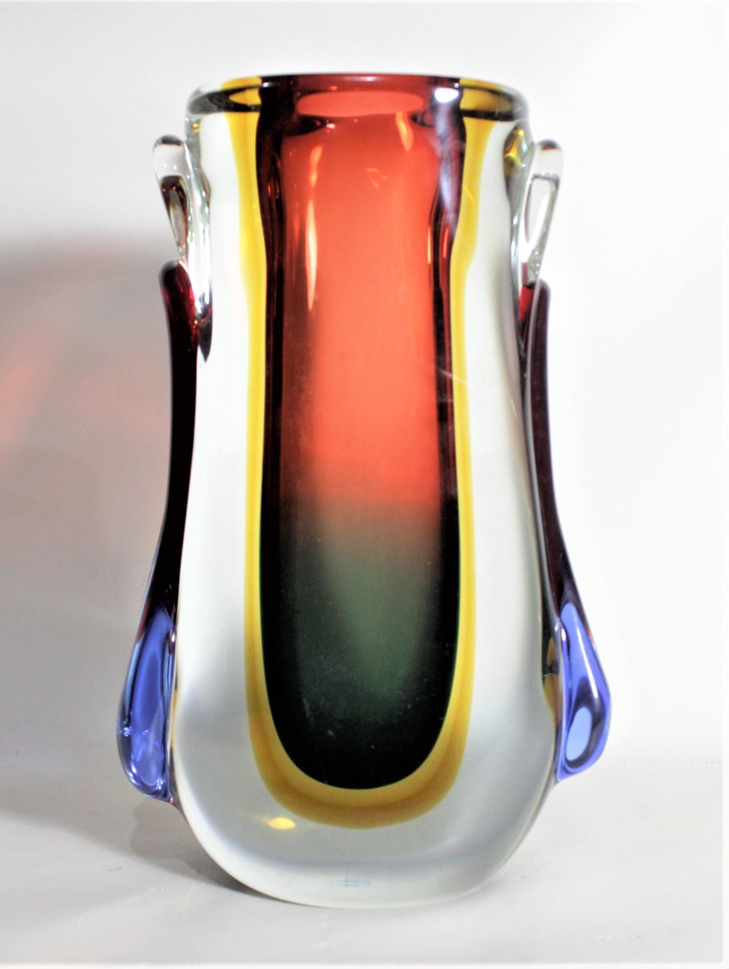 This midcentury art glass vase is unsigned, but presumed to have been made in Murano Italy in circa 1970 in the period midcentury style. The vase incorporates very thick and heavy clear glass with an inner layer of red to deep green surrounded by