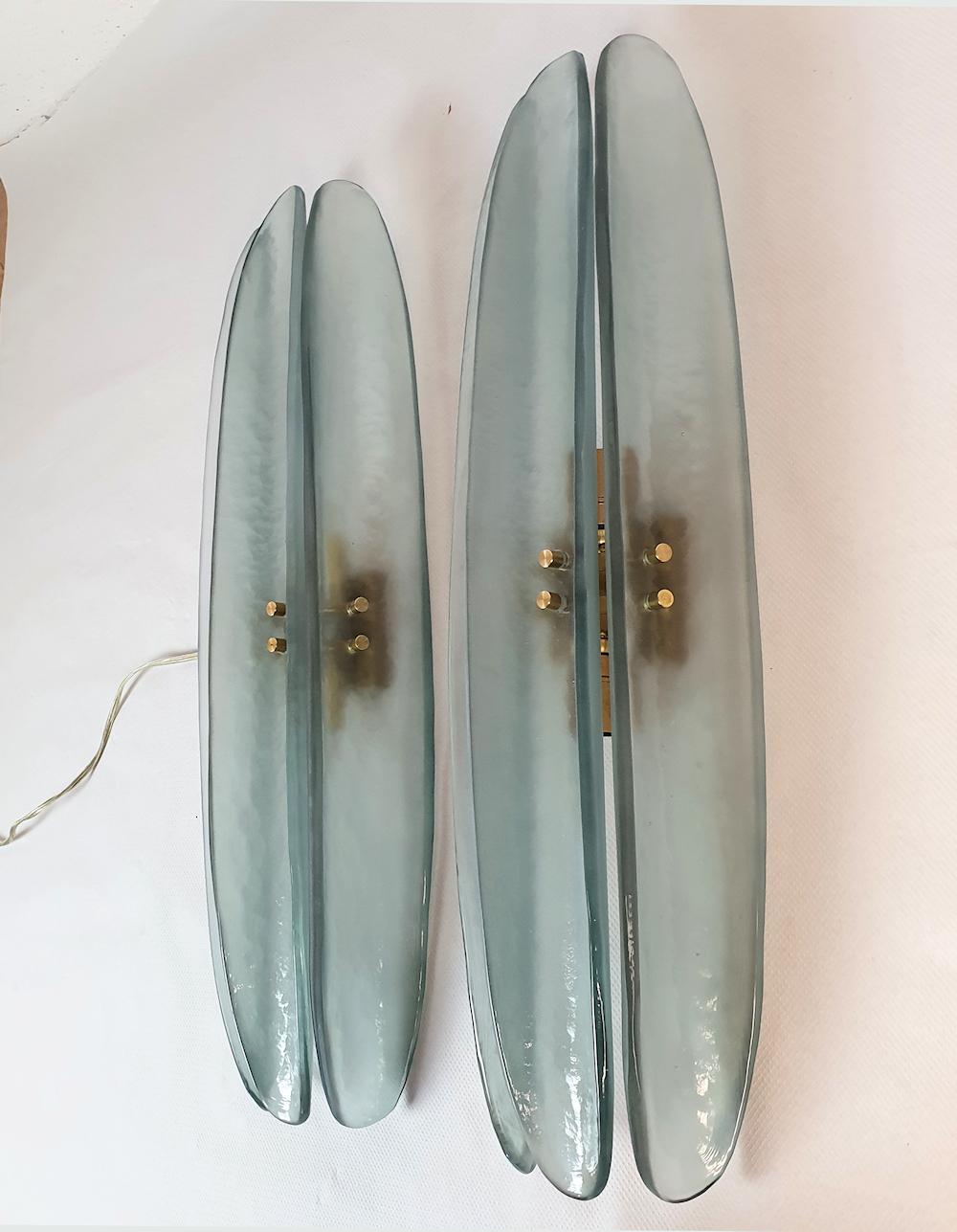 Mid-Century Modern pair of Murano glass wall sconces, attributed to Mazzega, Italy 1980s.
The vintage sconces are made of 3 long and curved tiles in Murano glass, in a beautiful semi-transparent blue/green color.
The sconces have 2 lights each and