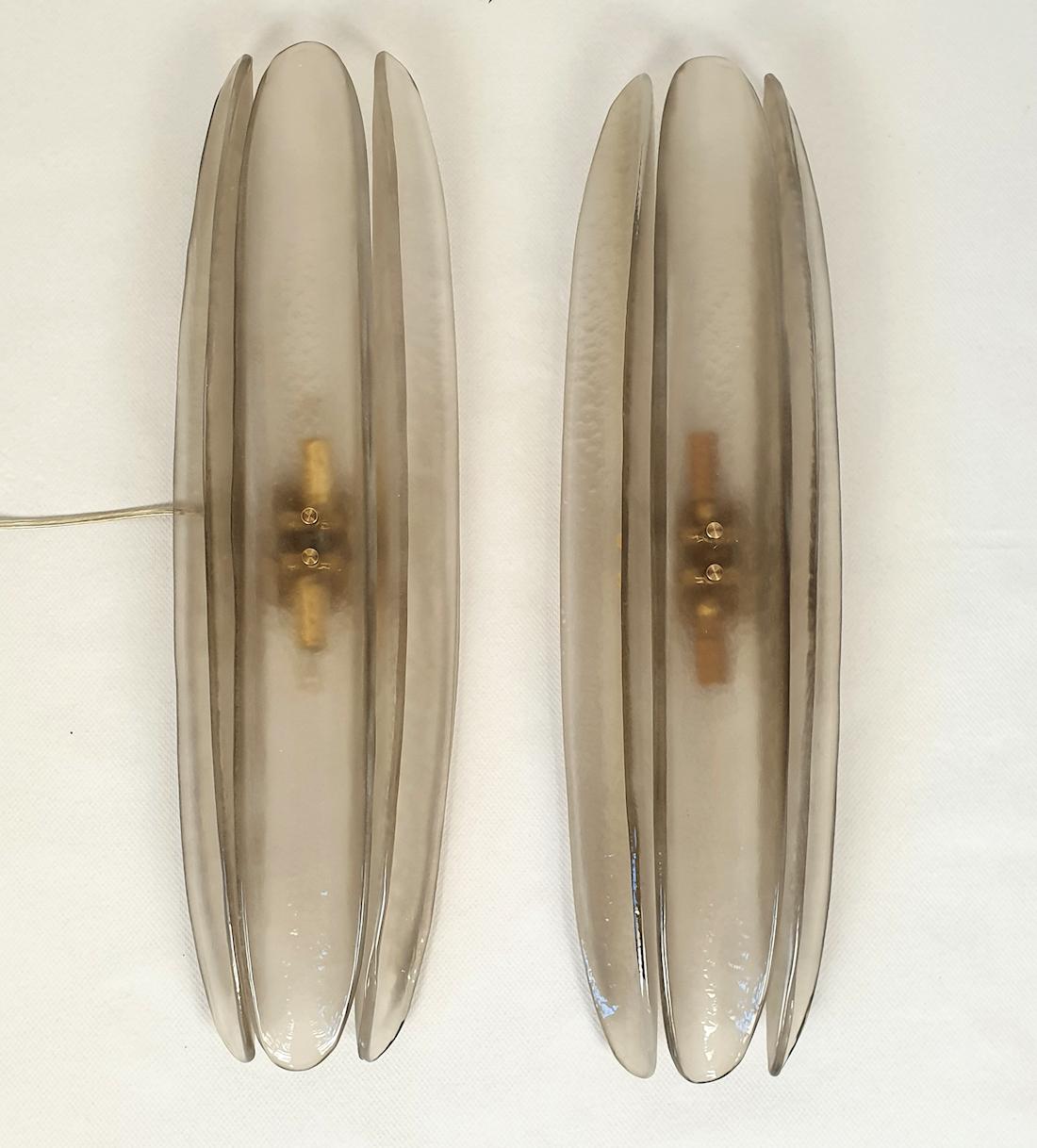 Mid-Century Modern pair of Murano glass wall sconces, attributed to Mazzega, Italy 1980s.
The vintage sconces are made of 3 long and curved tiles in Murano glass, in a beautiful semi-transparent taupe/sand color.
The sconces have 2 lights each and