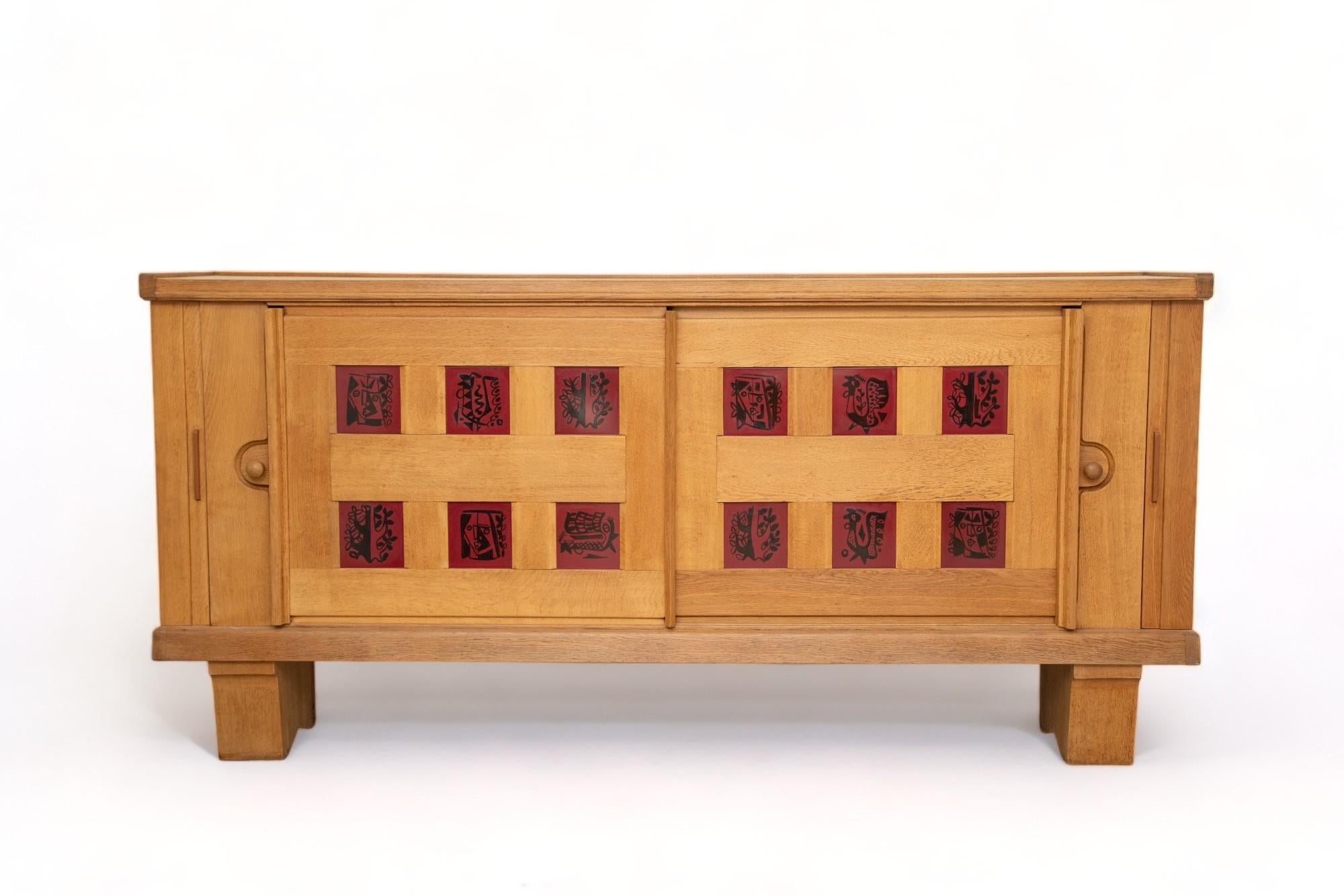 Large mid-century modern oak and ceramic sideboard
 by Guillerme et Chambron
Edition Votre Maison, France circa 1950-1960
 Opens with two sliding doors decorated by 12 burgundy and black ceramics by artist Boleslaw Danikowski
Concealing spacious