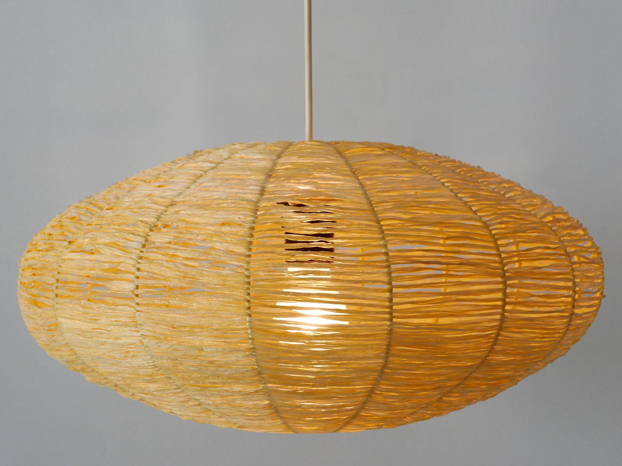 Rare, elegant and highly decorative Mid-Century Modern pendant lamp / hanging light. Manufactured in Germany, 1970s.

Executed in raffia bast and metal, the pendant lamp comes with 1 x E27 / E26 Edison screw fit bulb holder, is wired and in working