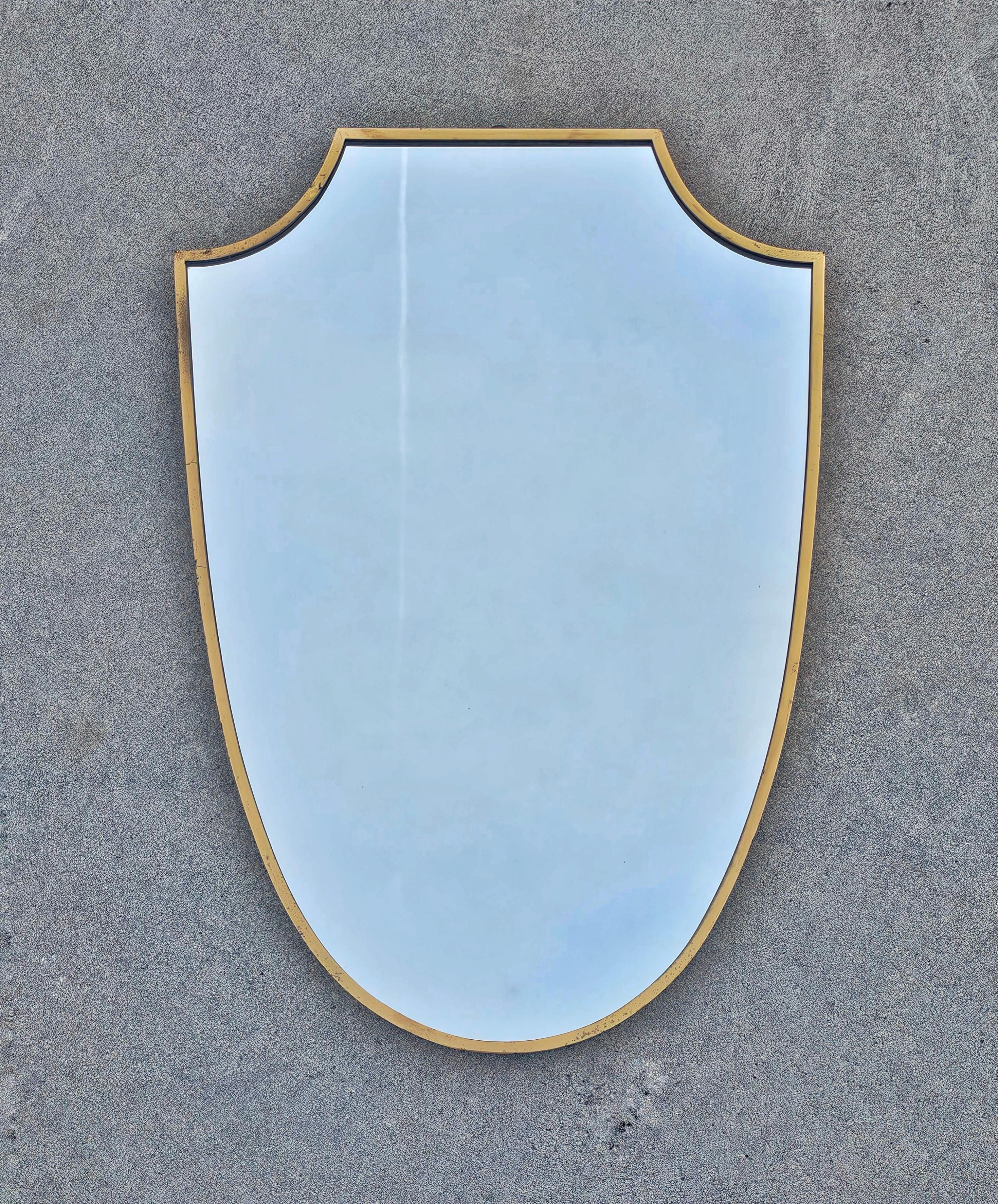 In this listing you will find a striking shield-shaped Mid Century Modern 
wall mirror in brass frame. Large format and gorgeous shape make this mirror a hard to find piece. On the back of the mirror you can still see the stamp saying 
