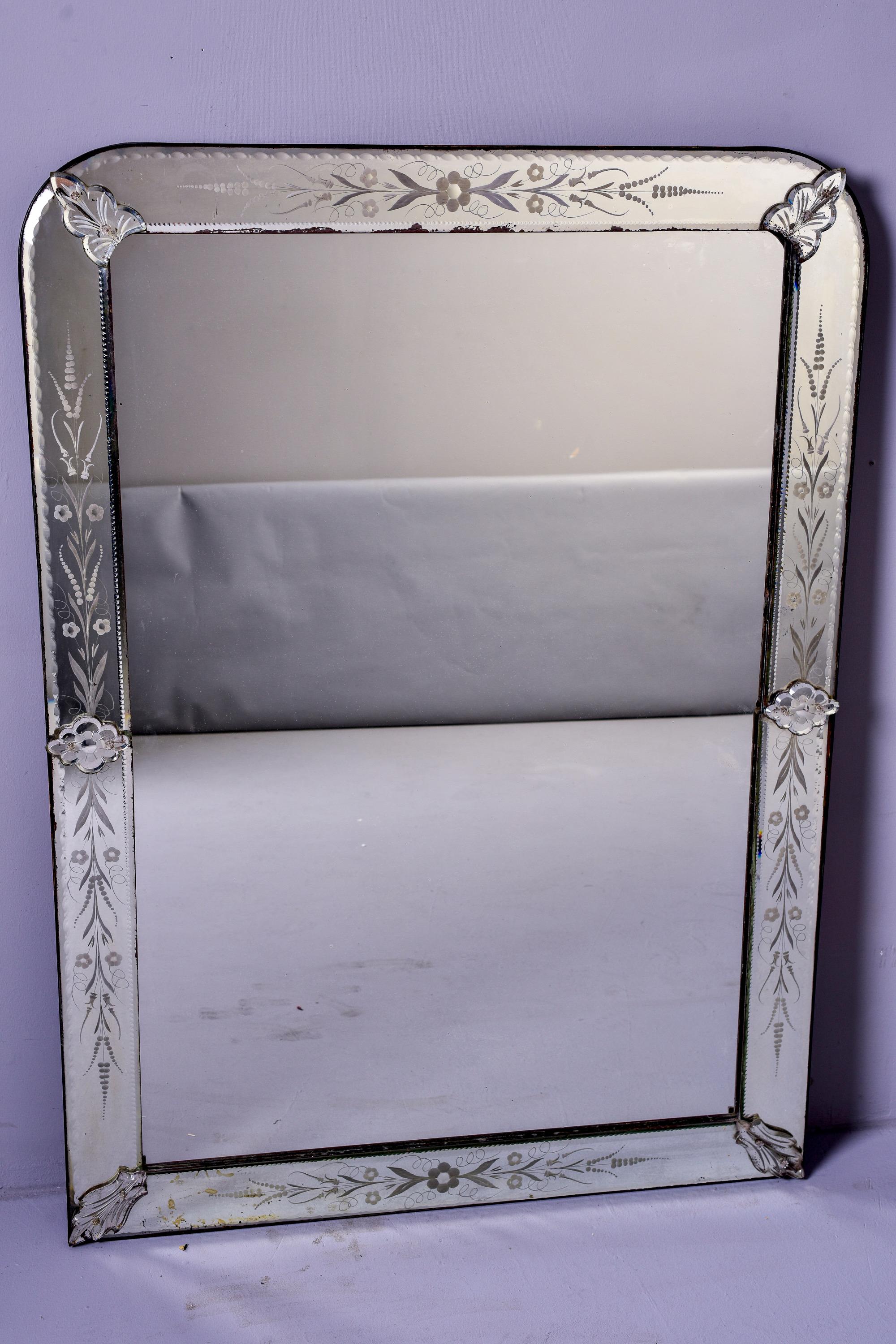 Circa 1930s / 1940s Venetian mirror features a mirrored frame with etched floral and vine details with a curved top and decorative borders on inside and outer edge. Unknown maker. 

Unframed mirror size: 44.25” high x 29.75” wide

Some