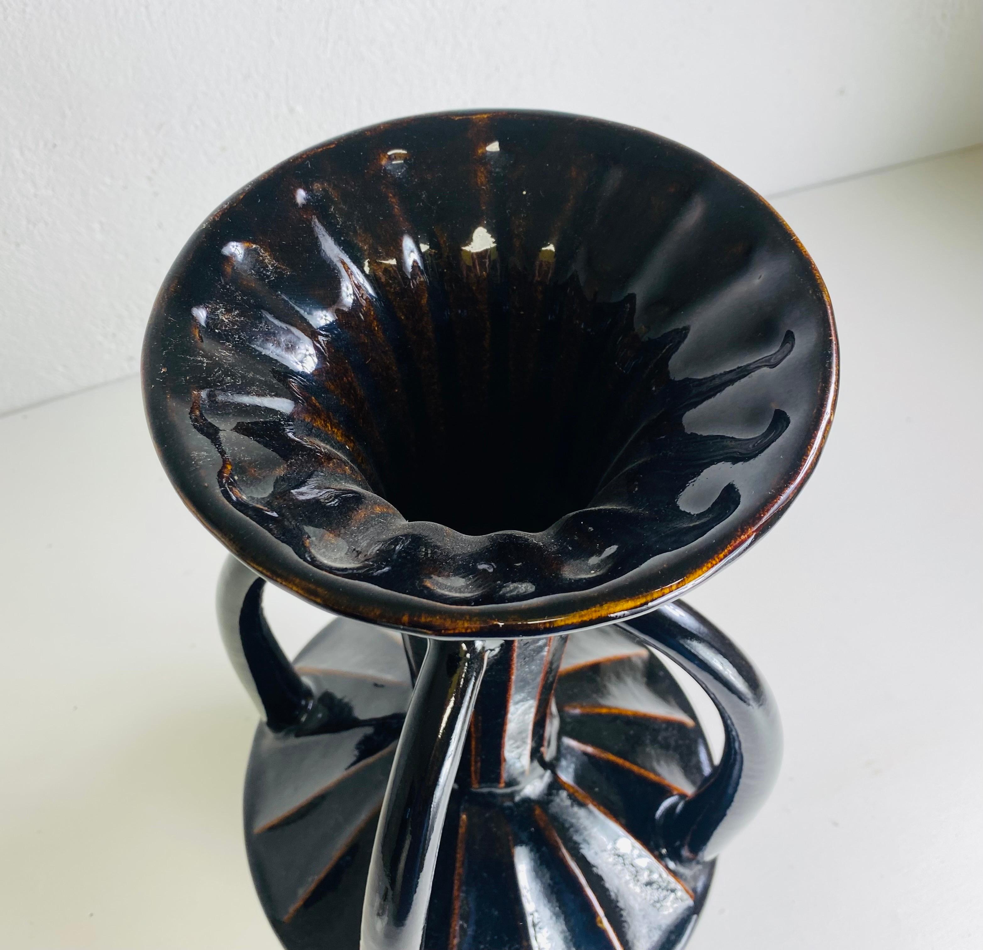 This is a large mid century vintage, espresso brown pottery vase. This vase features four large exaggerated handles with a ribbed detail to the center of the vase. This vase has a dark espresso brown glaze with an amber undertone.