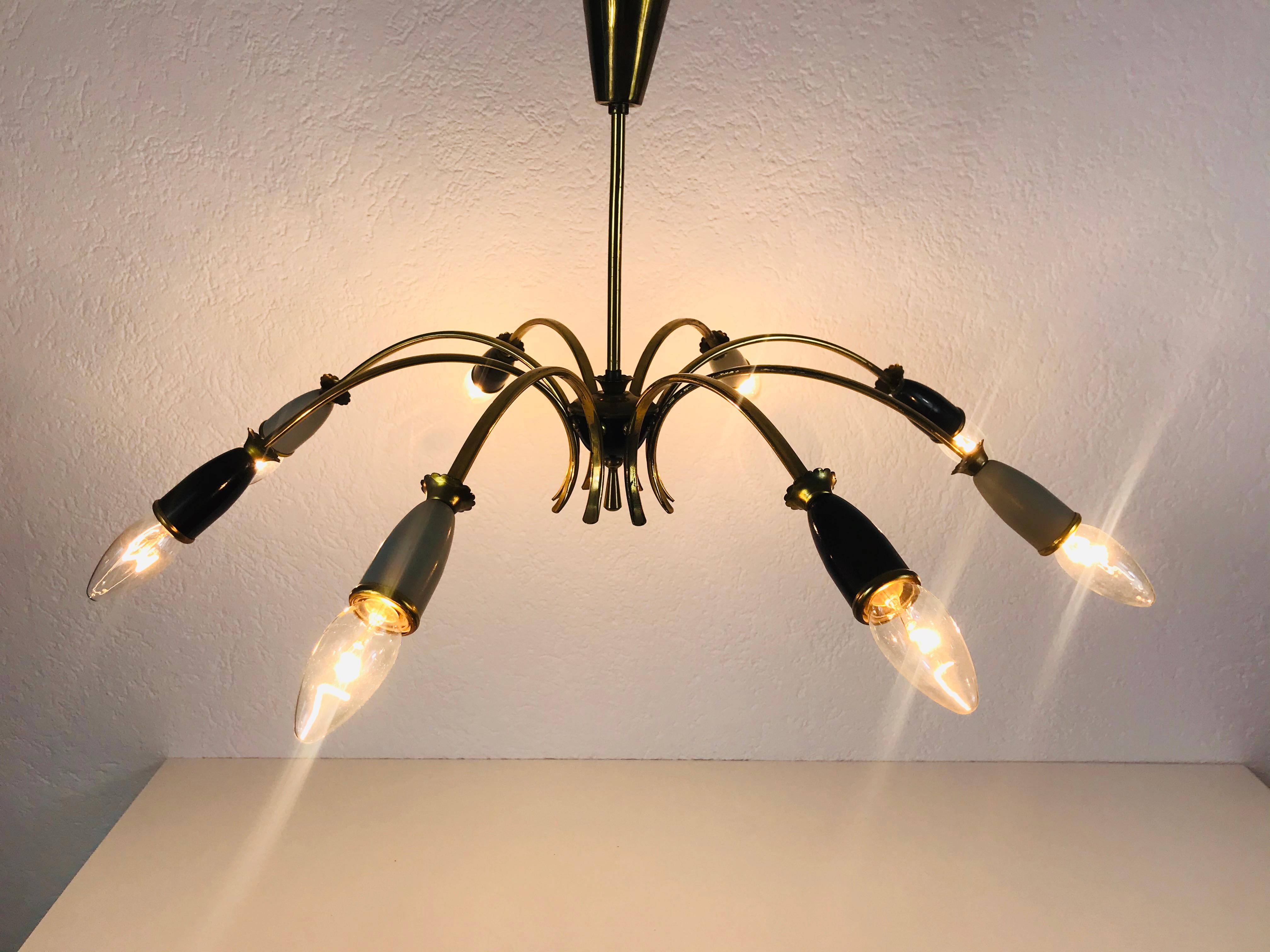 A Sputnik chandelier made in Germany in the 1950s. It is fascinating with its eight brass arms, each of it with an E14 light bulb. The arms have a grey and black color. The shape of the light is similiar to a spider. 

Very good vintage