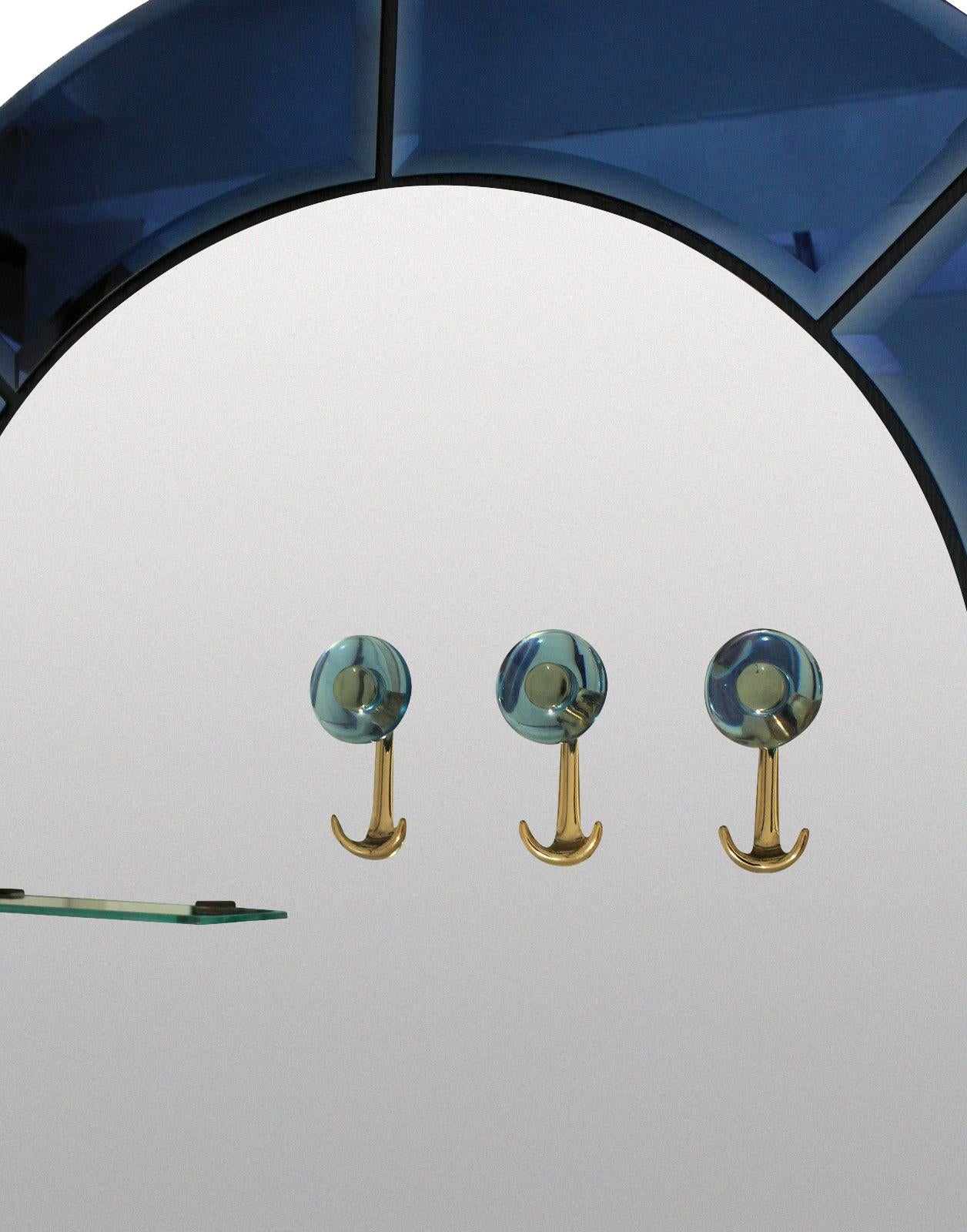 Grande specchio da sala o da toilette italiano della metà del secolo scorso con lastre smussate, bordate di blu e verde. Con due ripiani in vetro e tre appendiabiti in ottone.