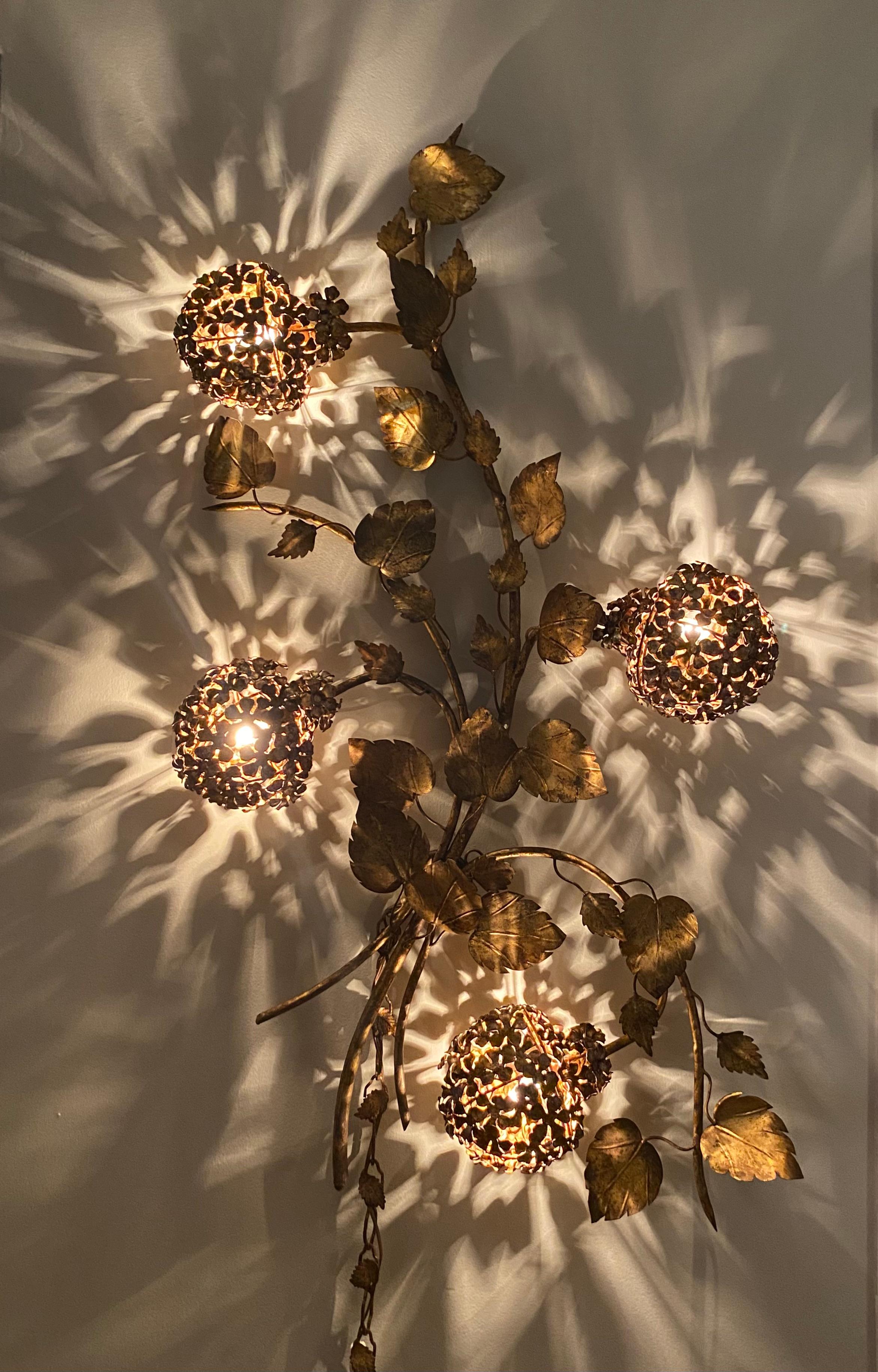 A glamorous gilded iron Italian tole wall sconce having lovely decorative leaves and designs depicting hydrangea's.  Attributed to Hans Kogl. 

When illuminated this light fixture displays very well and is eye-catching. 
Would enhance any modern,