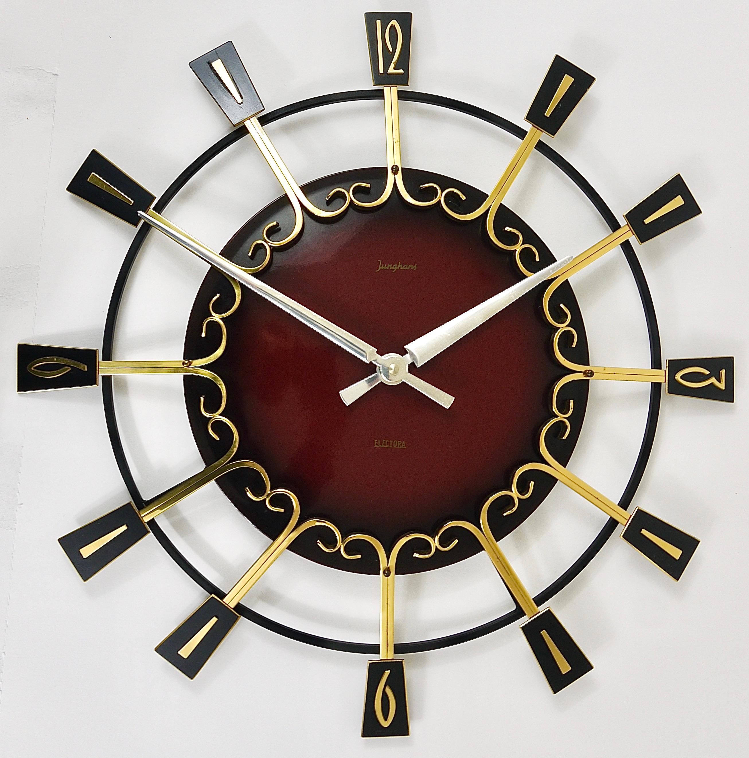 An impressive round Modernist Starburst Brutalism wall clock from the 1950s, executed by Junghans Germany. This clock has a diameter of 17.5 inches, its frame is made of polished brass and black-finished metal. It has a beautiful domed enameled