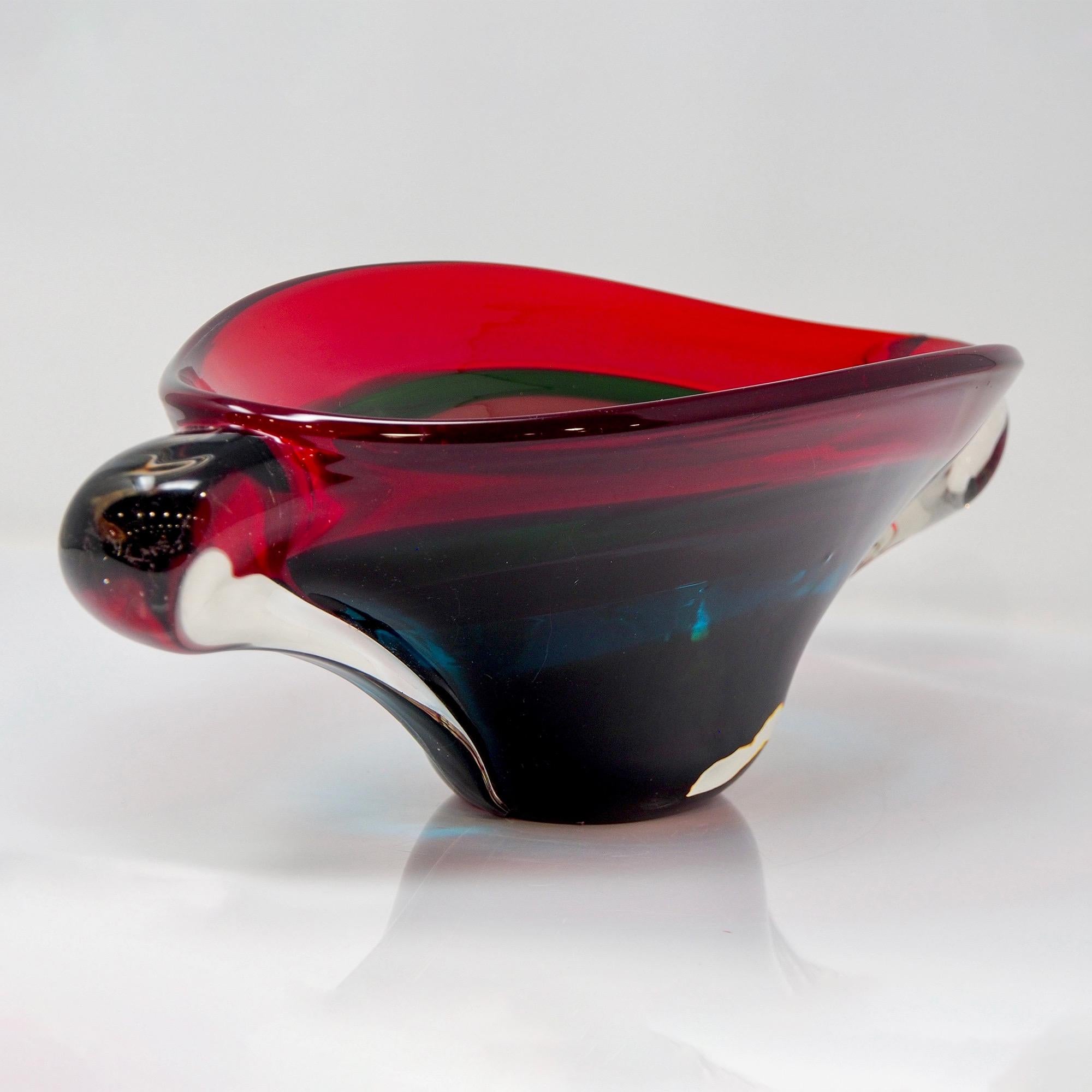 Circa late 1960s / early 1970s large mid century Murano glass center bowl features heavy glass of layered colors: red, green, smoky purple, blue and deep amethyst at the base with thick, clear winged handles at the sides. At just under 20” wide,