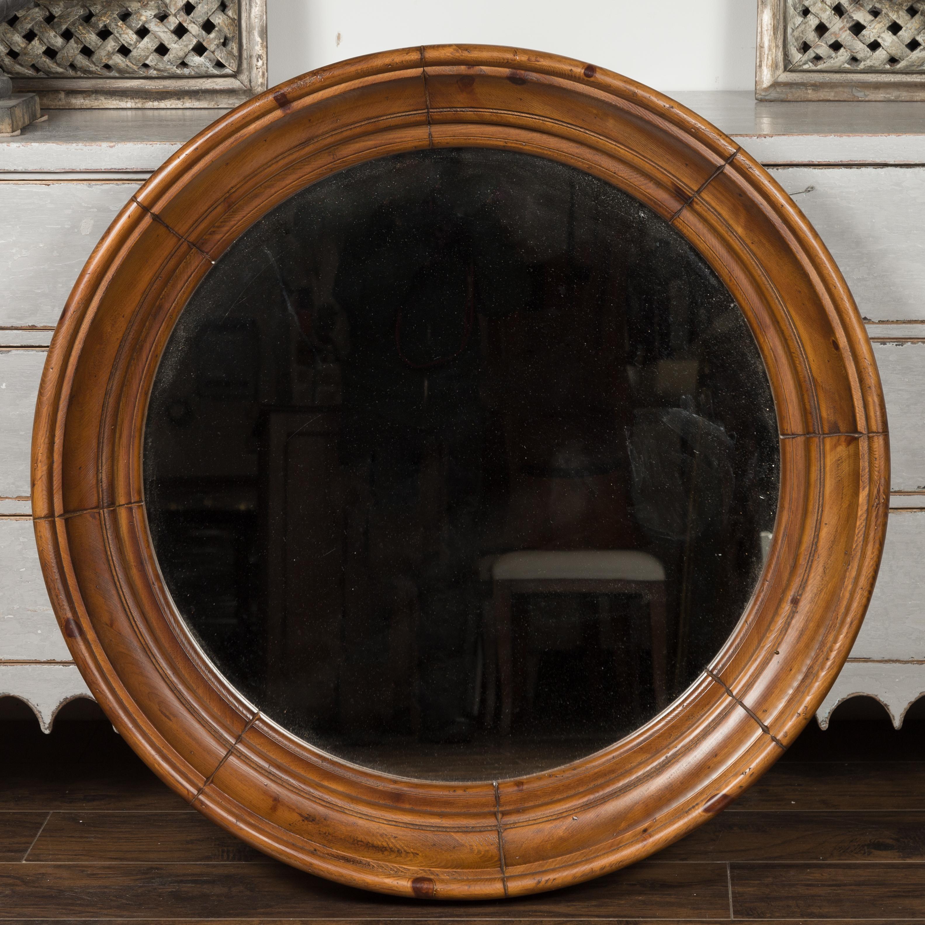A large vintage American pine bullseye mirror from the mid-20th century, with brown patina and clear mirror plate. Born during the midcentury period, this bullseye mirror features a brown pine molded circular frame surrounding a central flat mirror
