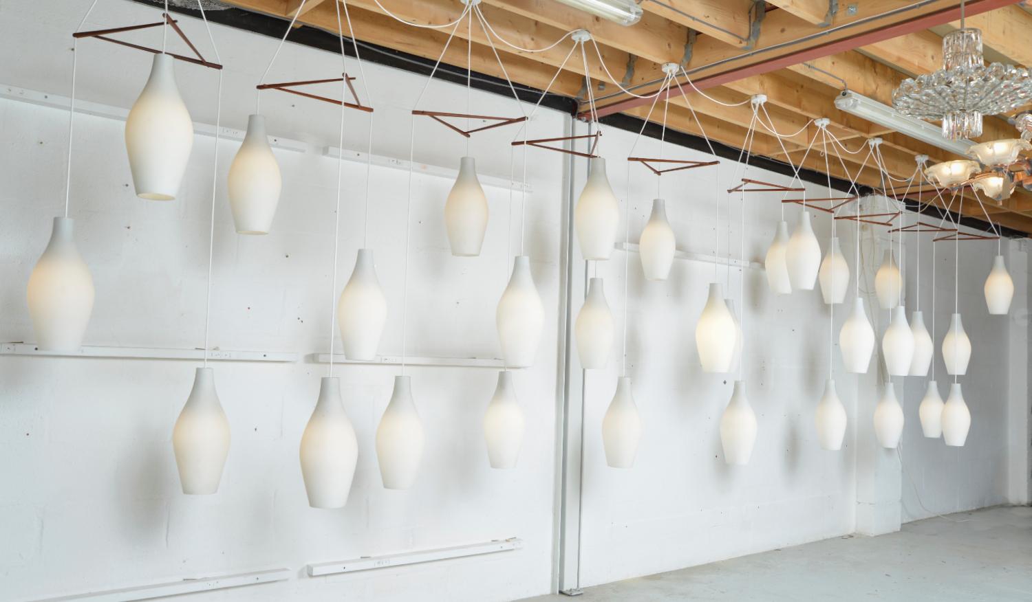 Un'impressionante serie di dieci grandi luci scandinave a cascata (ex edificio pubblico), risalenti agli anni '60. Ogni lampada ha tre bellissime gocce di vetro bianco smerigliato, appese a una struttura triangolare in teak. In totale ci sono 30