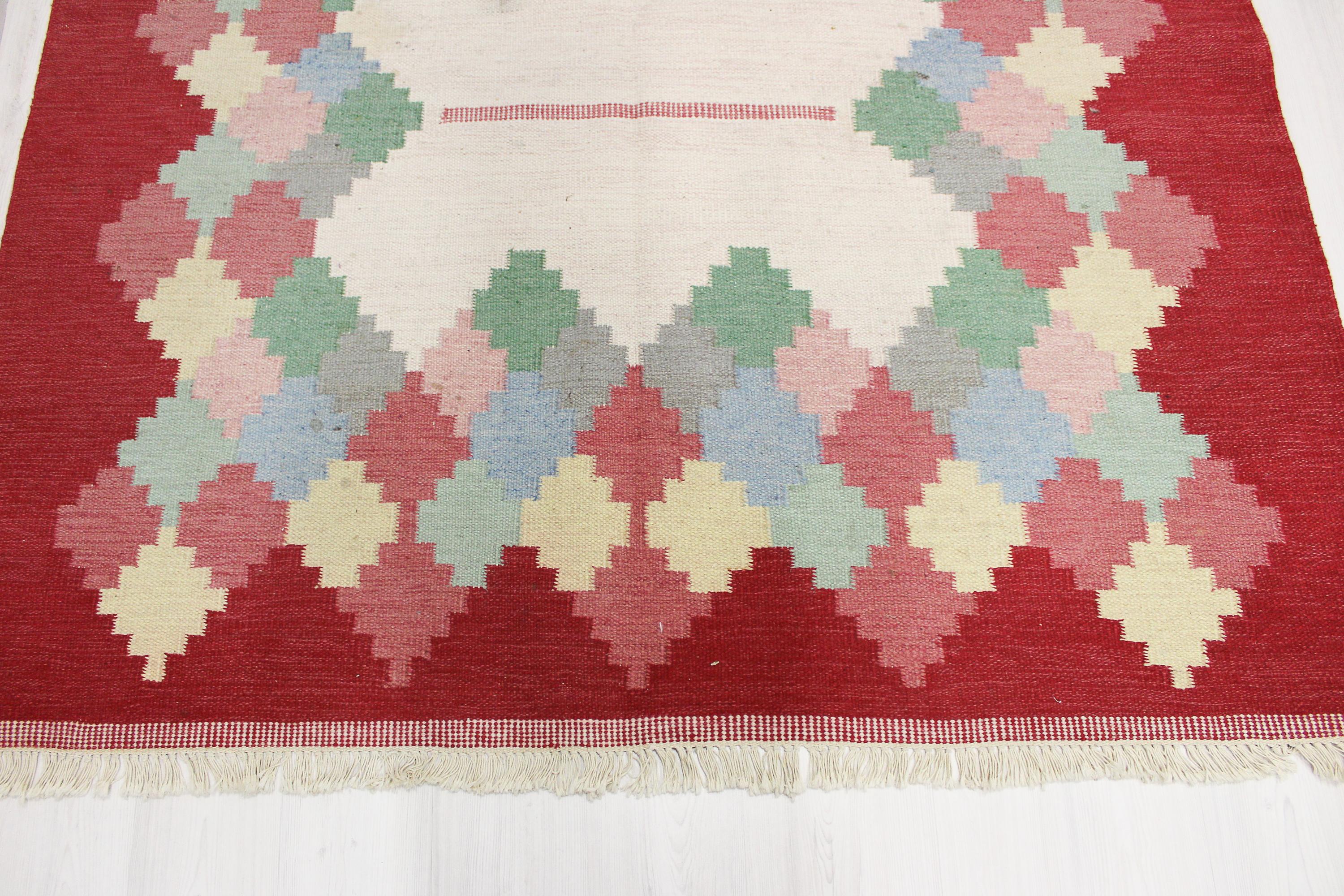 A large Swedish flat weave carpet by unknown designer. The carpet has a red and white base with multicolored geometrical patterns. Very good vintage condition with some smaller stains (should be easily removed when washed).