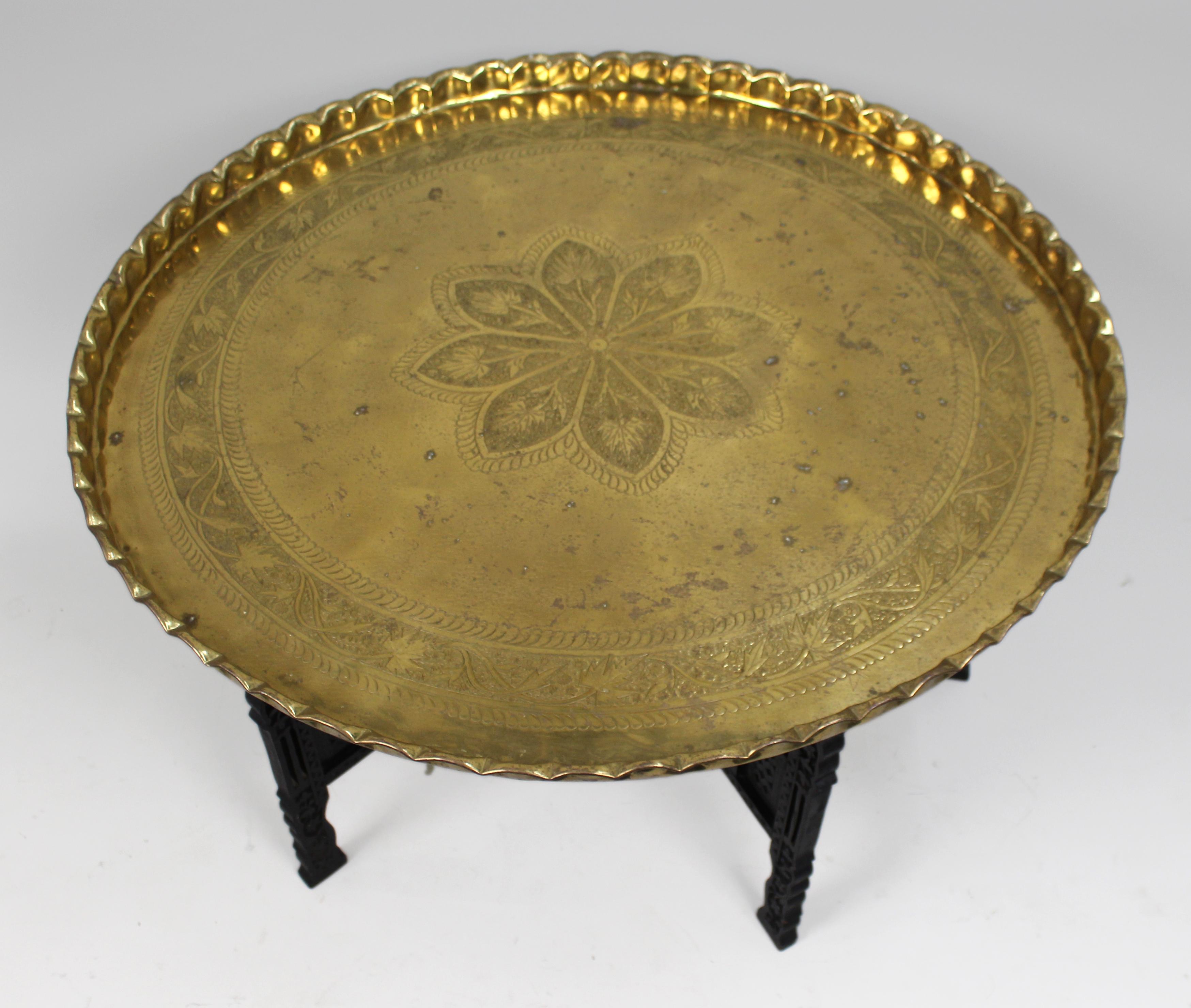 Large Middle Eastern Brass Tray Table on Carved Hardwood Folding Stand
Mid 20th century

A fine and generously sized decorative brass tray table, likely Moroccan or Middle Eastern in origin, dating from the mid 20th century.

The circular brass tray