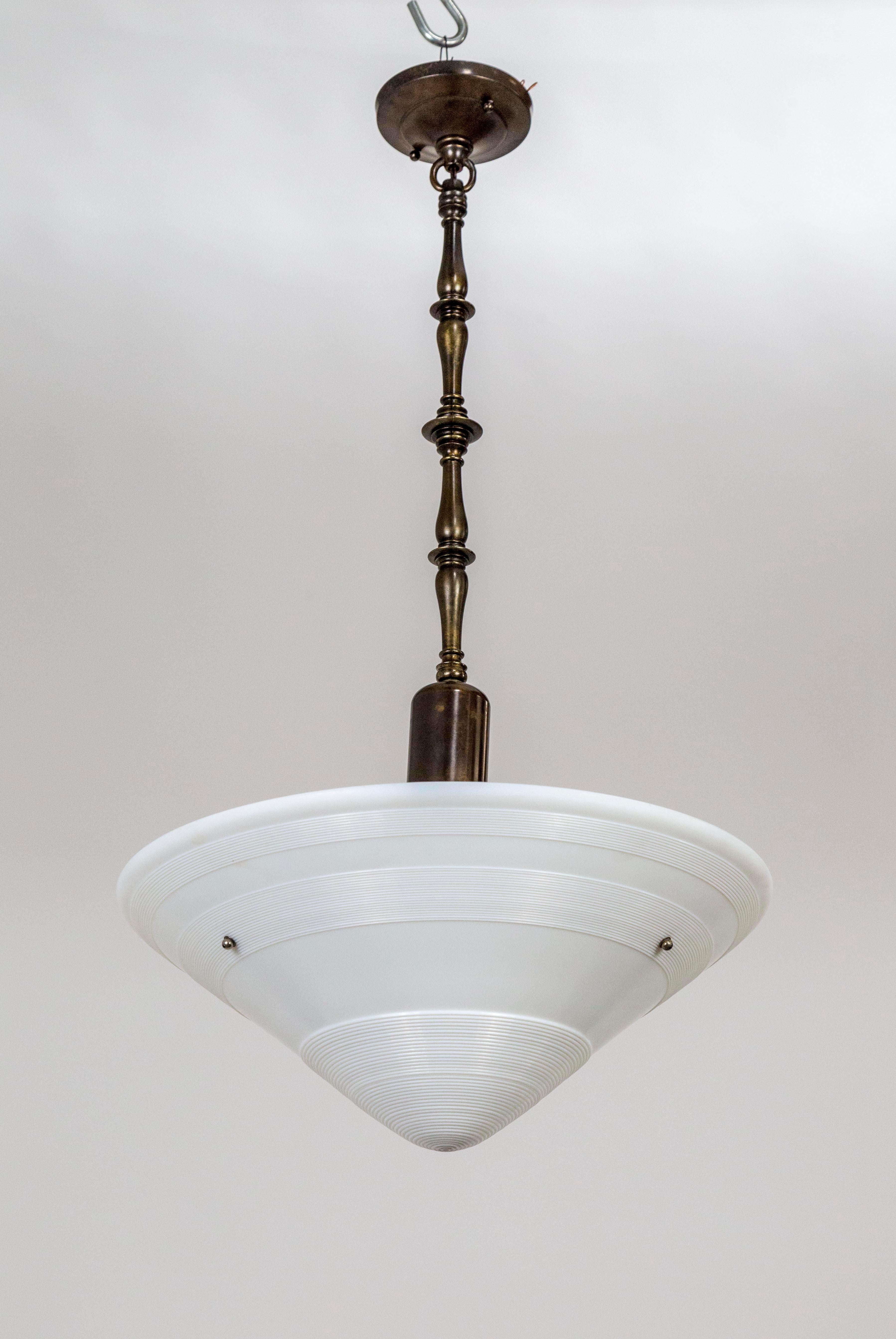 A pair of newly fashioned, Art Deco pendant lights with milk glass cone shapes suspended from decorative, turned style, brass stems in an oil rubbed bronze patina. The glass is textured with intricate ribbing wrapped in stripes around the cones.