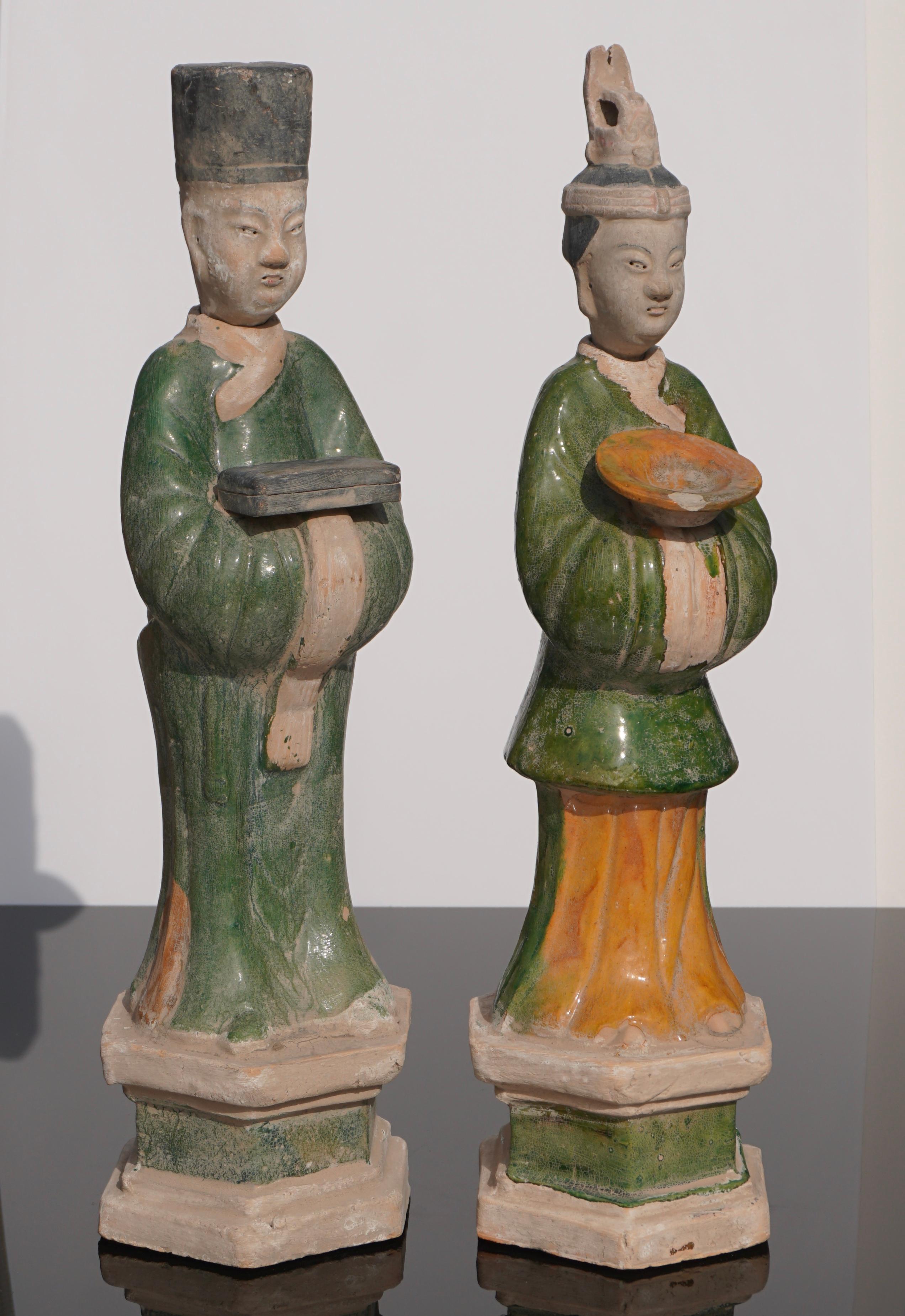 These two Sancai glazed figures in particular are distinguished by their dress, for each wears a unique robe and hat, and by the objects they carry in their arms (one holds a box, the other a bowl). As Chinese statuette art prescribes, the faces are