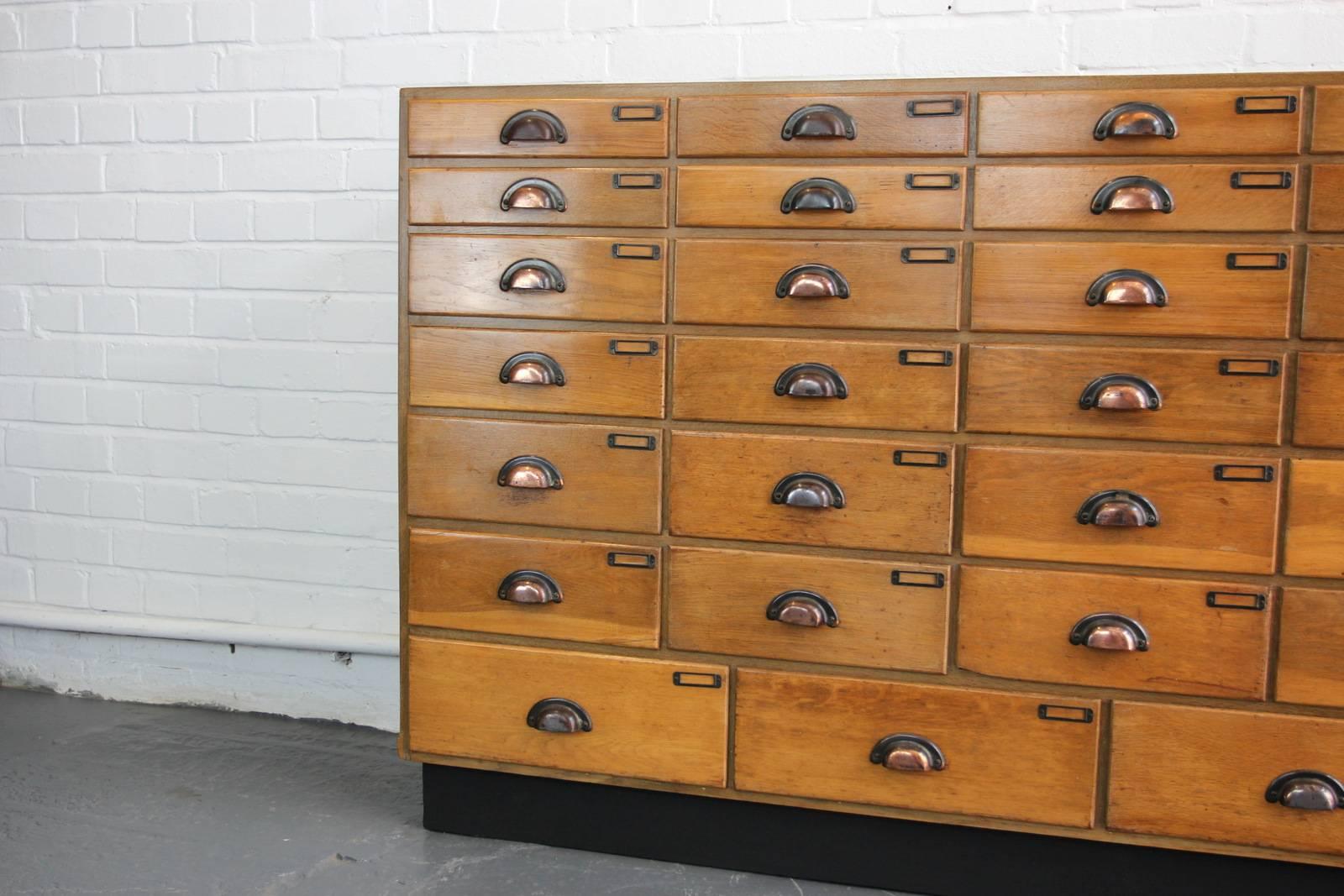 Large mirror fronted haberdashery drawers, circa 1930s.

Product code #OA525

- Original copper cup handles and card holders
- Solid oak 
- Original makers badge
- Mirrored front
- 34 drawers
- English, circa 1930s
- Measures: 182cm long x
