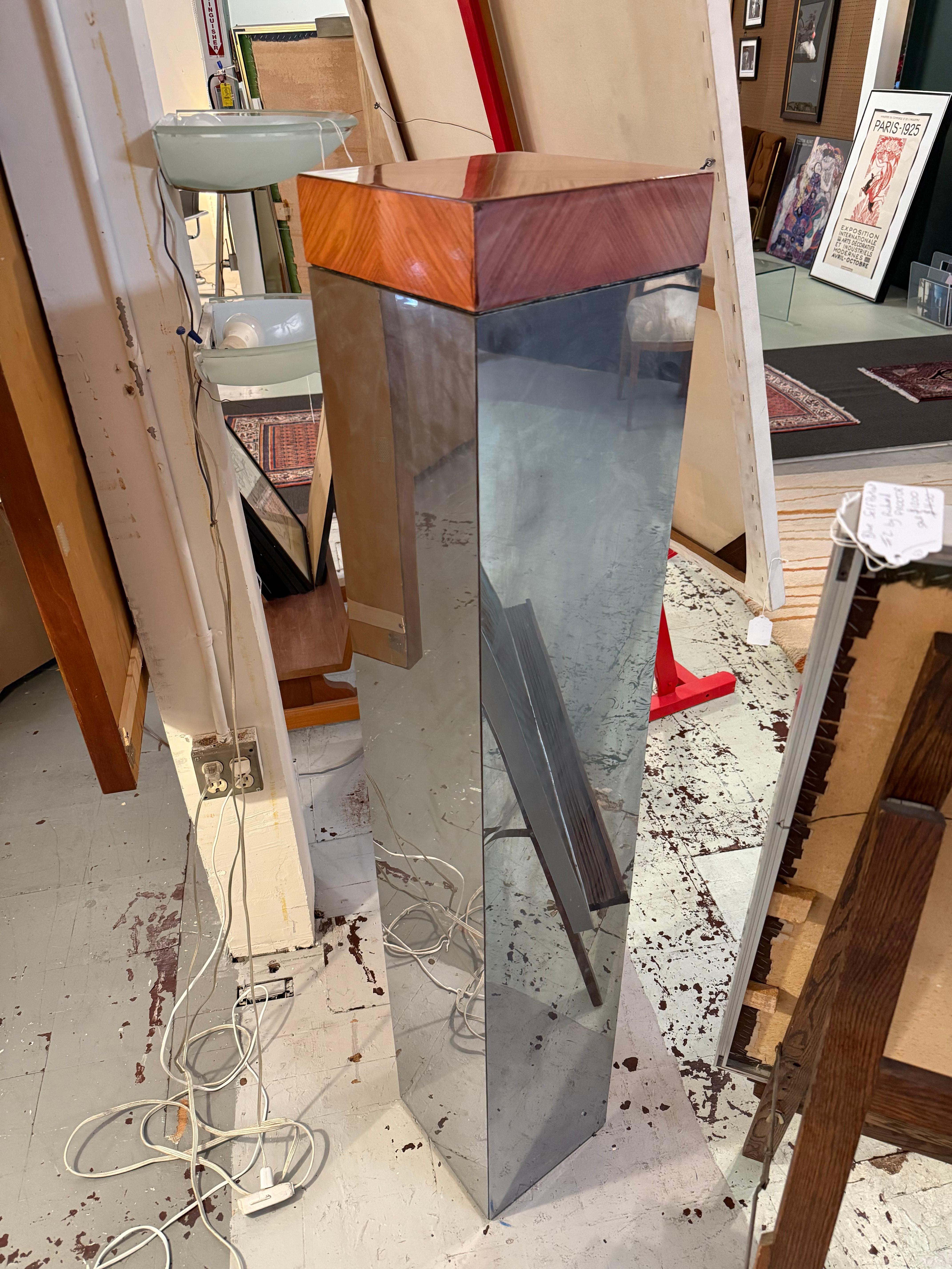 Cette étonnante colonne haute associe un corps en miroir réfléchissant à un plateau en bois chaleureux, créant ainsi un contraste sophistiqué entre modernisme froid et texture organique. La forme effilée met l'accent sur la hauteur et la