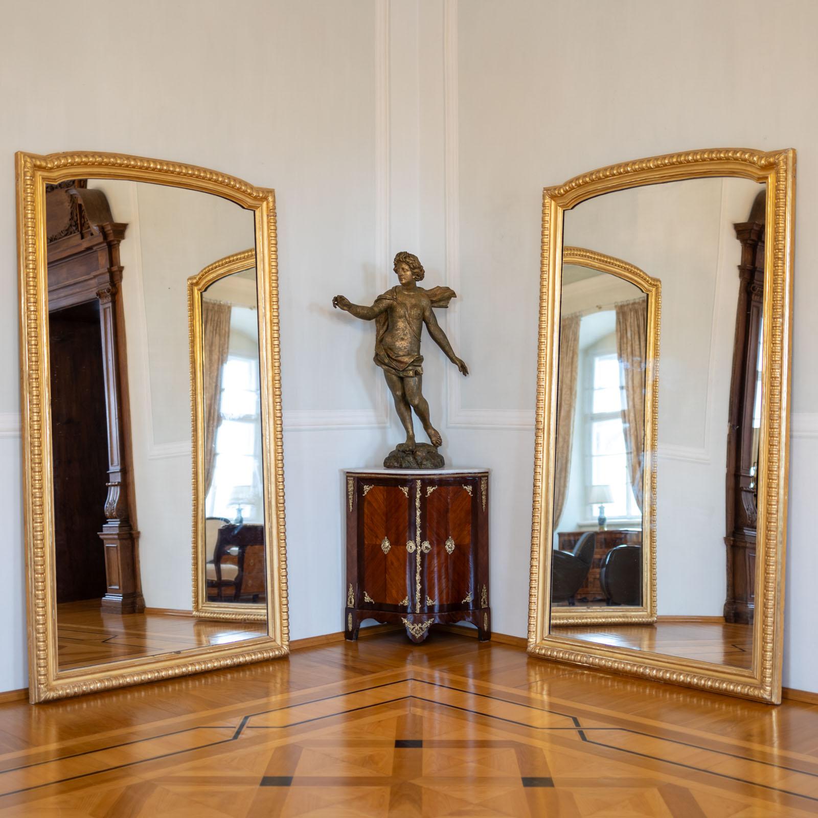 Pair of large hall mirrors in a gold-patinated frame with arched top and old mirror glass.