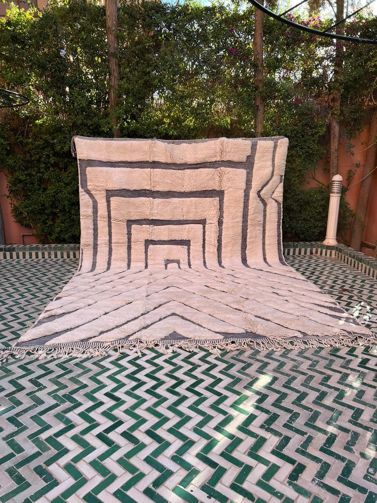 Ce grand tapis marocain crème tissé à la main a été réalisé sur un métier à tisser traditionnel par des artisans qualifiés dans les montagnes de l'Atlas. Il est fabriqué avec de la laine M'Rirt ultra luxueuse et de haute qualité. Il s'agit d'une