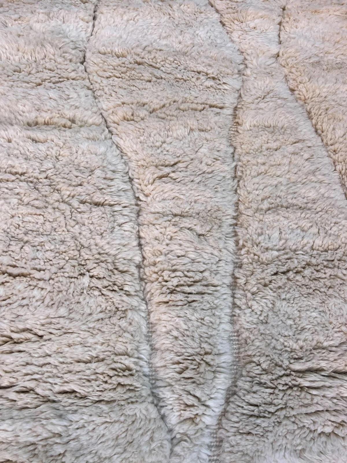 Ce très grand tapis marocain blanc tissé à la main a été fabriqué à la main par des artisans qualifiés dans les montagnes de l'Atlas. Fabriqué à la main avec de la laine M'Rirt ultra douce et de haute qualité, il constitue la pièce d'apparat neutre