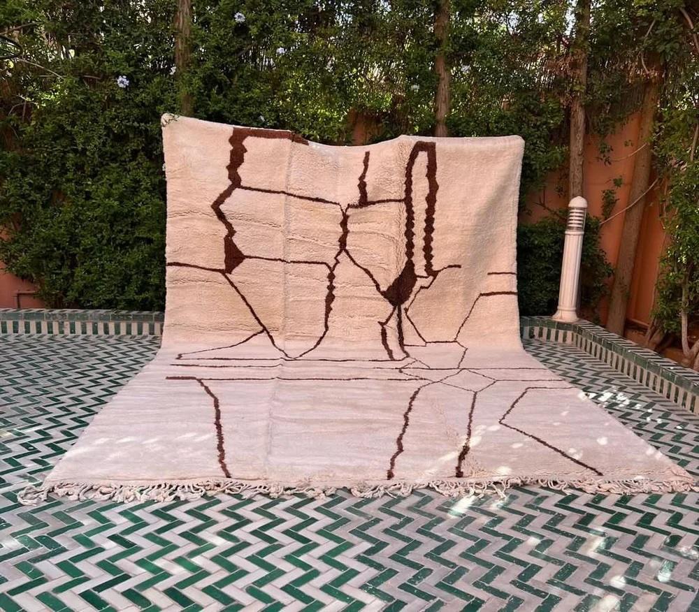 This large, modern handwoven Moroccan rug was made by hand by skilled artisans in the Atlas Mountains. It features a high quality, neutral cream wool base with a graphic, rich brown abstract design unique to Moroccan style. Handmade on a loom using