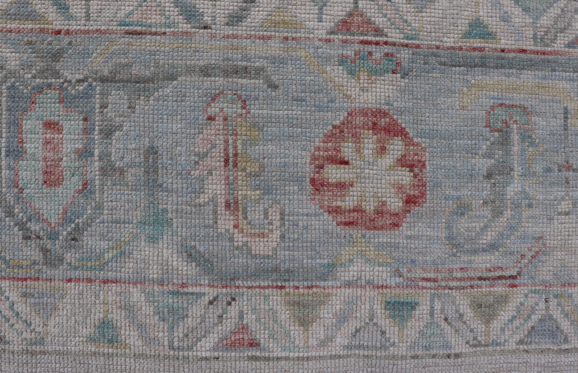 Large Modern Oushak with floral design on light blue/gray border with pops of color. Keivan Woven Arts; rug AWR-9004 Country of Origin: Afghanistan Type: Oushak Design: Mosaic Floral, All-Over. 21st century.

Measures: 10'1 x 13'10.

The field is