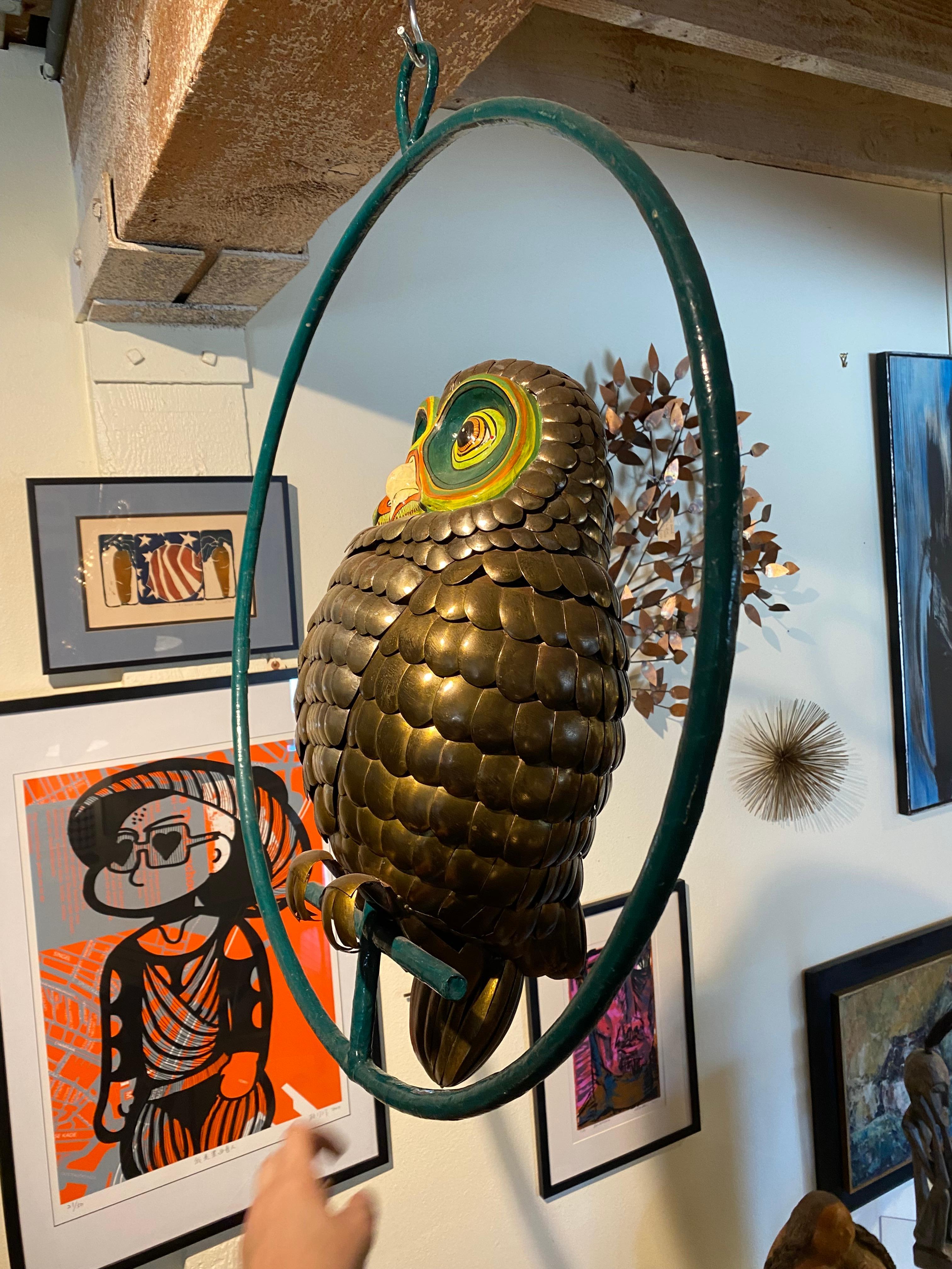 Perched on a thin crossbar, this owl sculpture made by Sergio Bustamande stares at the viewer with painted eyes, their spiraling, hypnotic contours. The green and gold of its gaze suggest a supernatural watchfulness, as though observing from an