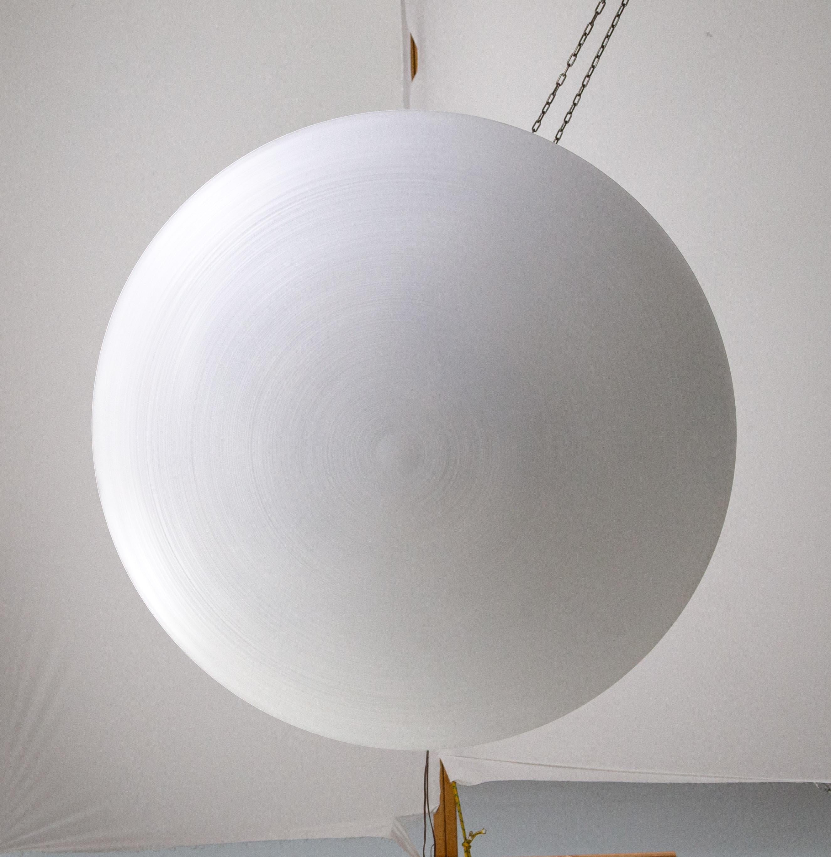 A large, matte-white, spun aluminum, convex disk up-light fixture in a minimal, modern design. It hangs roughly 8 inches from the ceiling to cast a pleasing, diffused light. It is versatile and complements many styles. Made in California by Nova