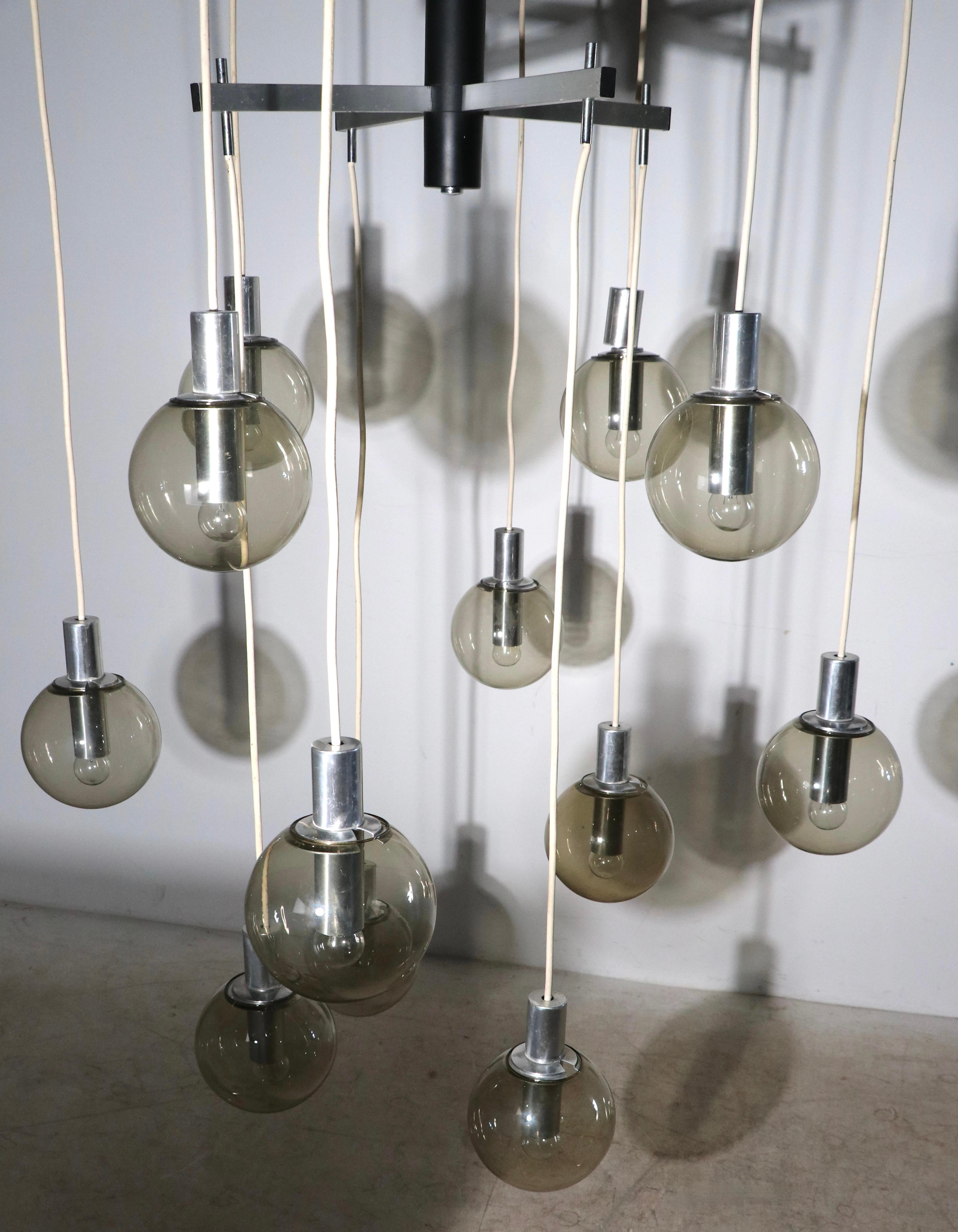 Impressive modernist chandelier having three tiers, of four globes each, with a total of twelve hanging globes. The fixture has a center pole shaft of steel, in black finish, from which radiate twelve rectangular aluminum arms , each supporting a