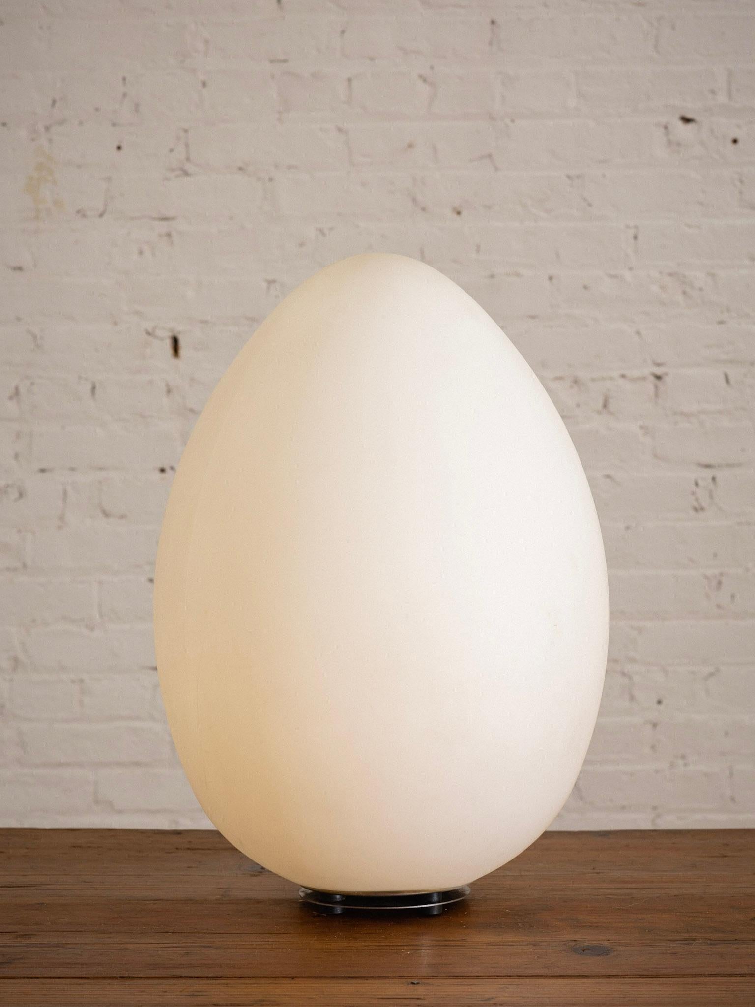A large molded plastic egg form lamp. Frosty white in color. Emits a warm glow when lit. Chrome disc base. Standard US lightbulb can be replaced by removing the base with and allen wrench. Pair available, sold separately.