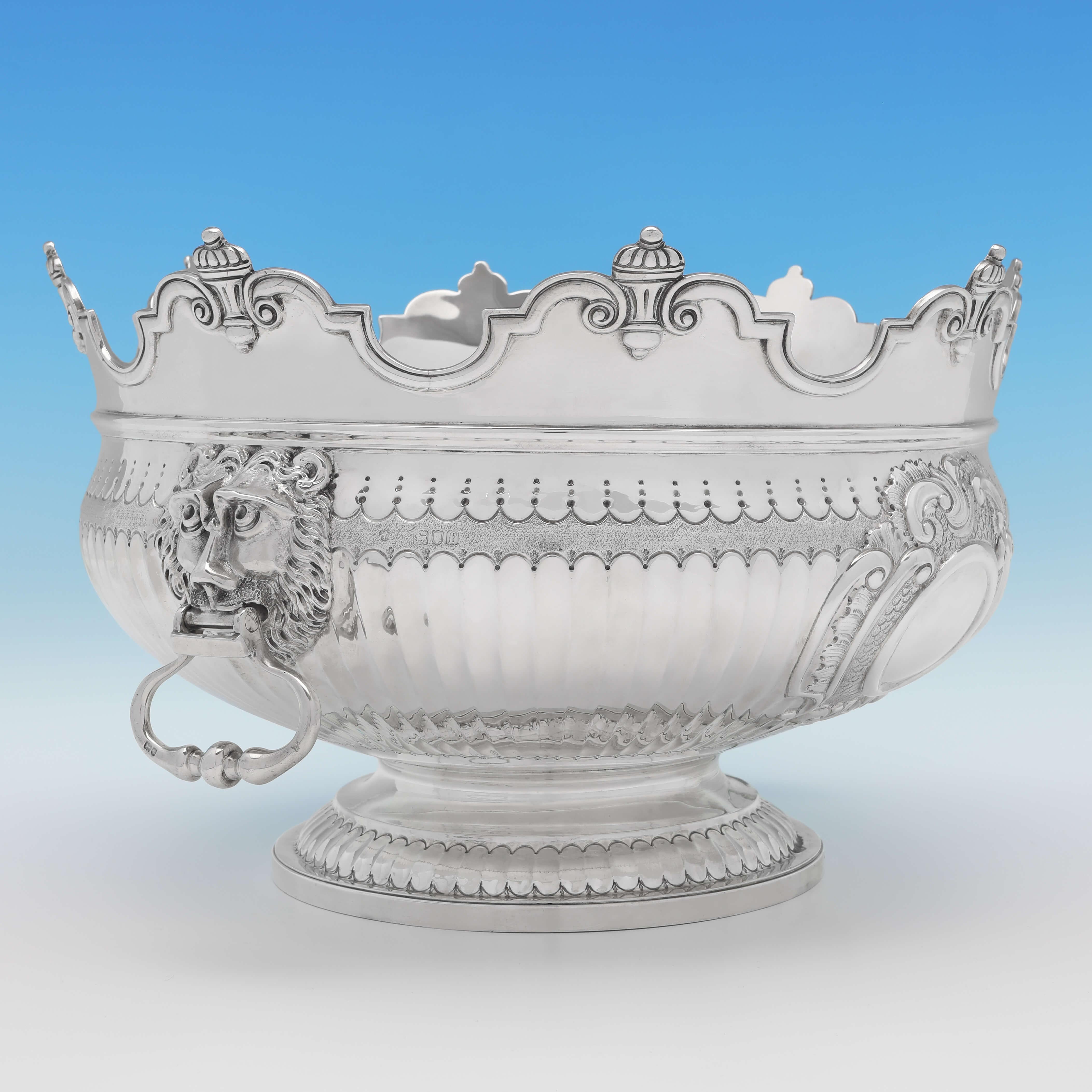 Hallmarked in London in 1901 by Charles Stuart Harris, this very attractive, Victorian, antique sterling silver bowl, features a Monteith style rim, lion mask drop ring handles, and engraved chased decoration throughout. The bowl measures