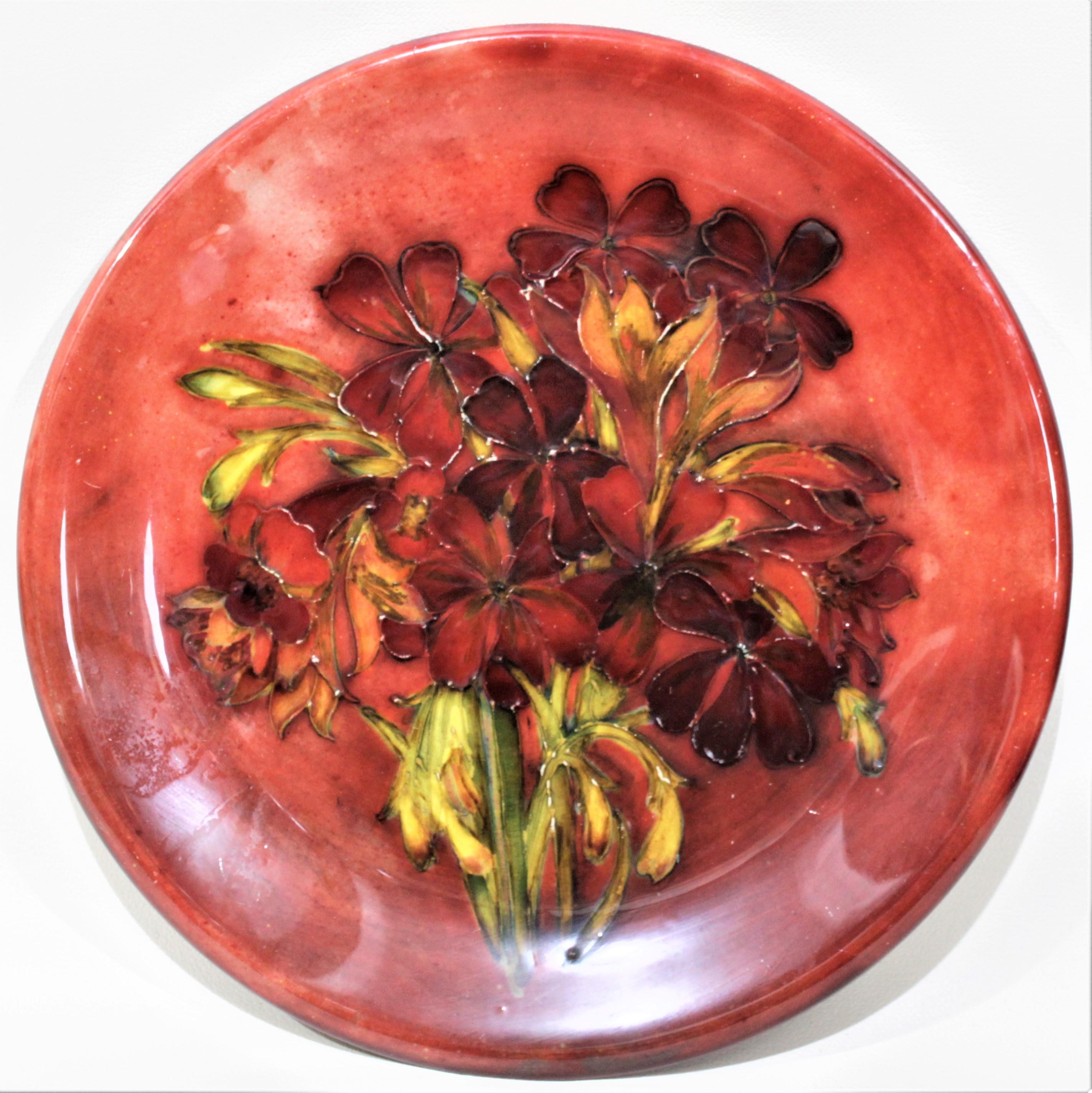 This large Moorcroft charger was made in circa 1940 with a deep flambé glaze in the 'Spring Flowers' pattern. The top of the plate is hand painted with a large bouquet of deep red flowers and green stems and foliage with yellow highlights. The depth