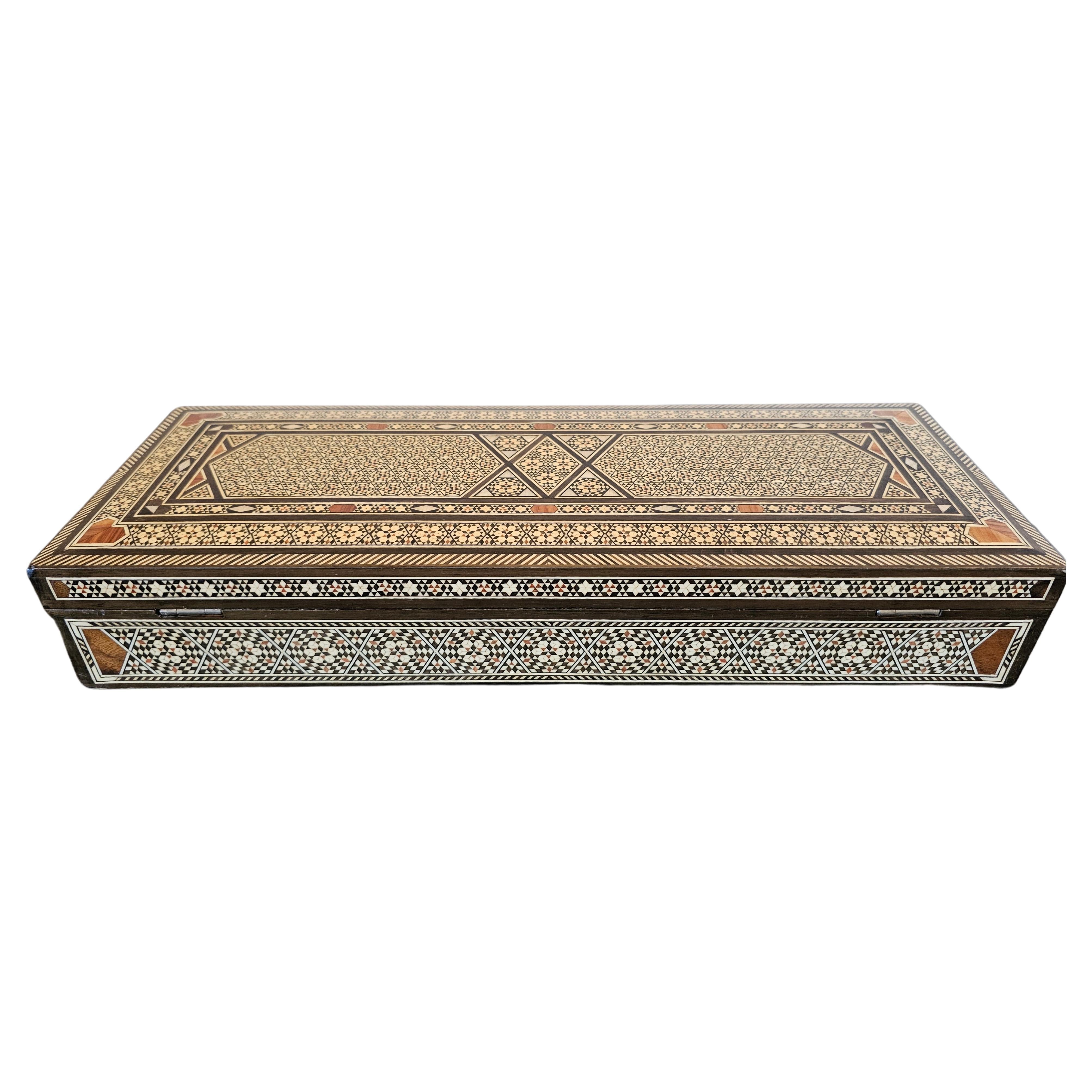 A stunning vintage Moorish arabesque inlaid table box, 20th century, high quality rectangular box with hinged lid, featuring contrasting mother of pearl, exotic hardwood, and bone marquetry inlay arranged in geometric patterns, opening to red fabric