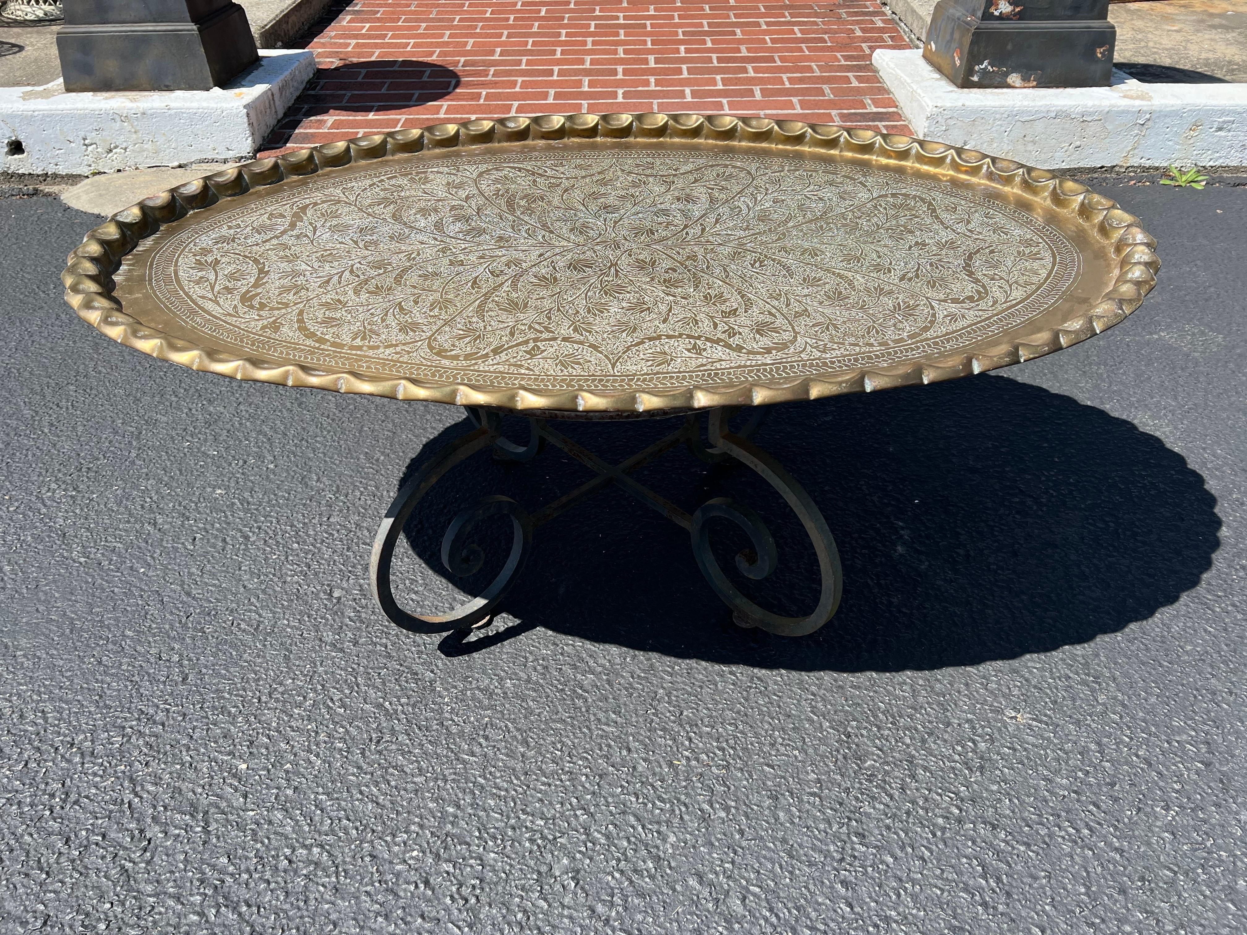 Large Moroccan brass tray table. Heavily embossed large oval tray table with incredible hand hammered edge that rests upon a forged iron base. Perfect oval shaped coffee table. Easy to move in or out doors.