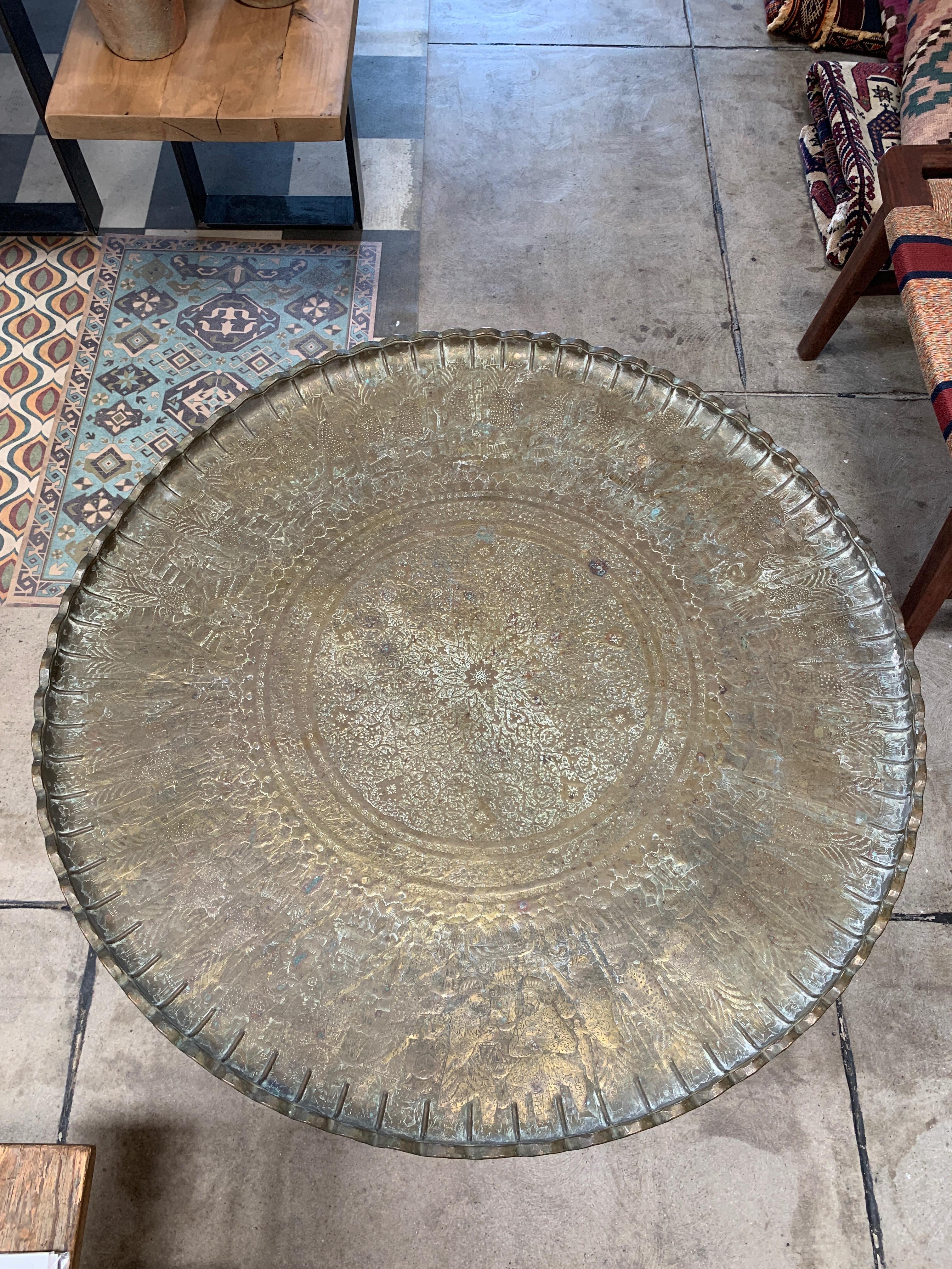 This vintage Moroccan brass tray table retains all of its Art Deco style character. All the fixings are completely original. The brass is carved with intricate designs of men, animals and patterns that, once polished to a shine, make this table an