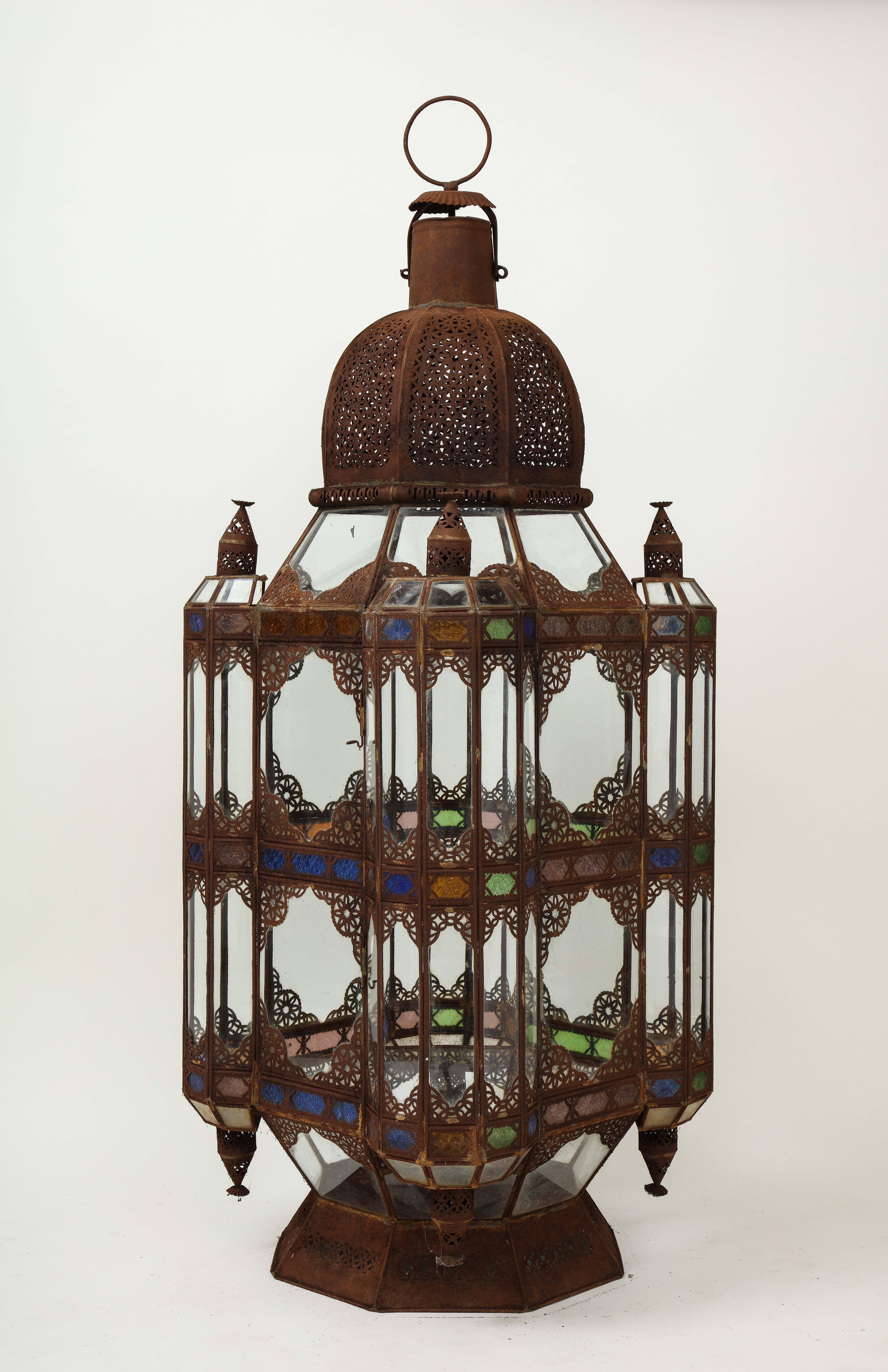 Impressively large hurricane lantern with patinated metal filigree frame inset with green, blue, amber and clear glass.