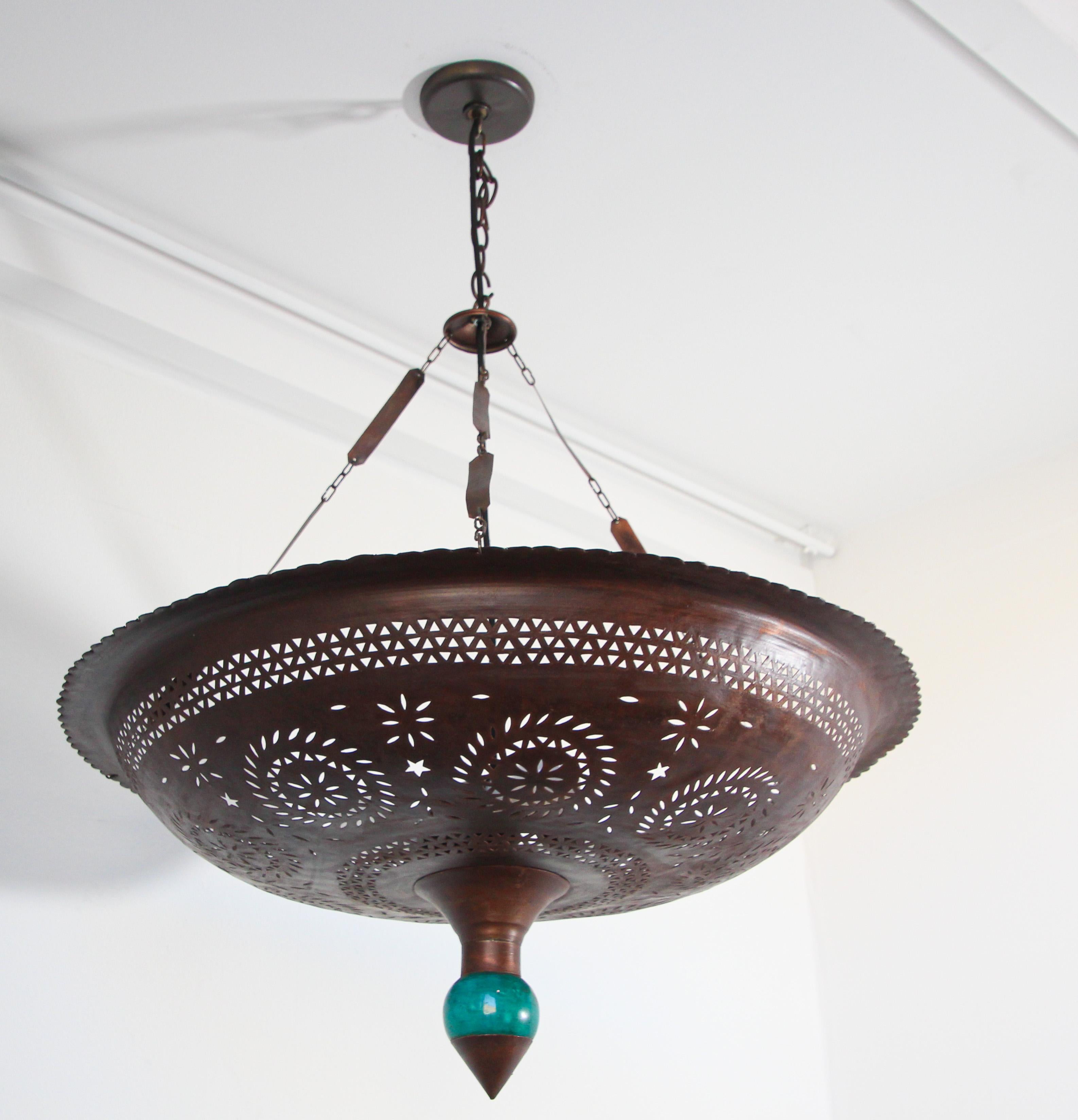 Large vintage Moroccan handcrafted hanging metal ceiling light with nice intricate geometric Moorish cut-out and a blue teal turquoise ceramic porcelain final.
The cut out of this large ceiling pendant light will creates a sole uplight that