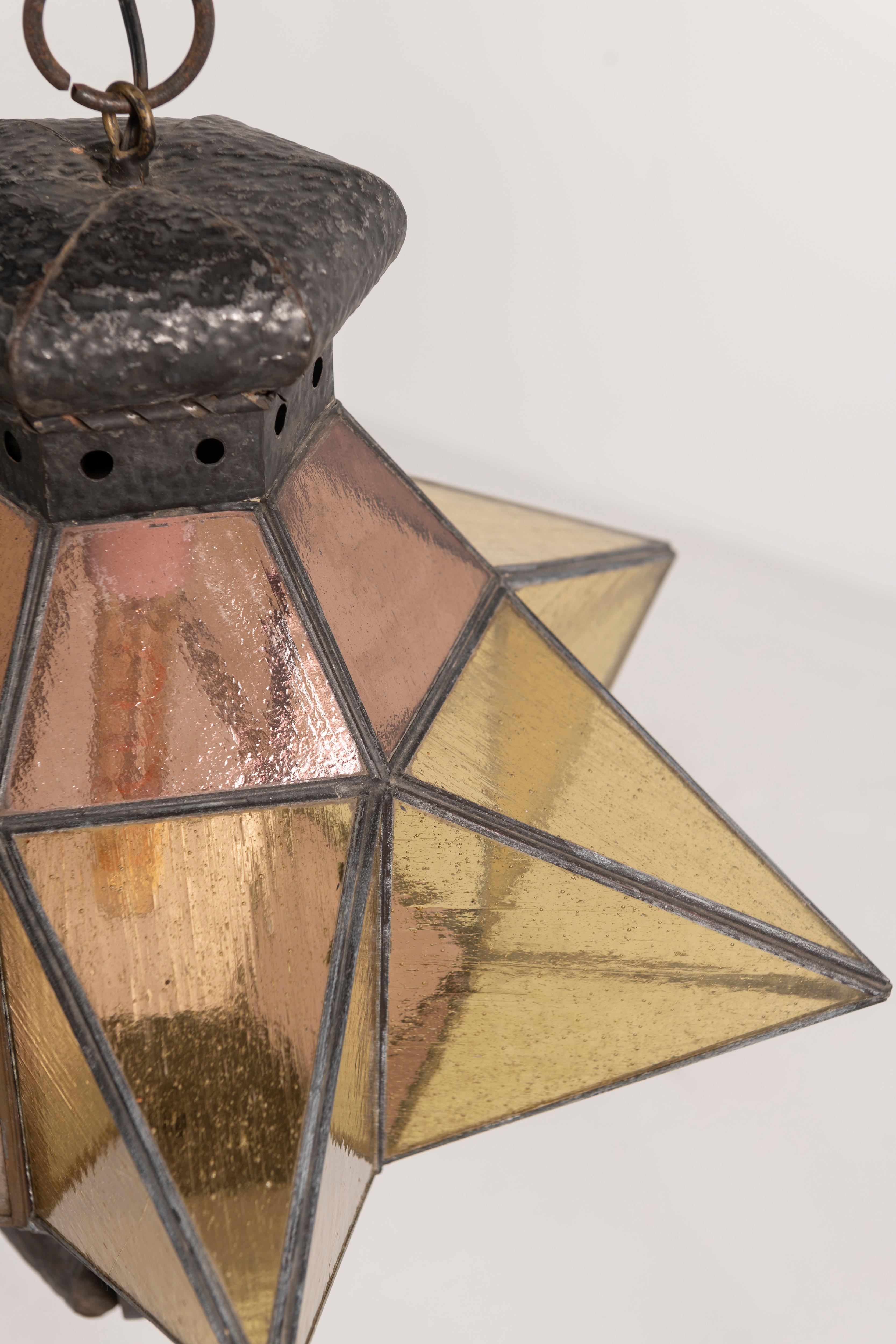 Ce remarquable pendentif marocain en forme d'étoile, fabriqué en fer forgé et en verre soufflé, fusionne les techniques artisanales traditionnelles avec une esthétique moderne. La lampe crée une ambiance subtile avec des nuances douces et tamisées