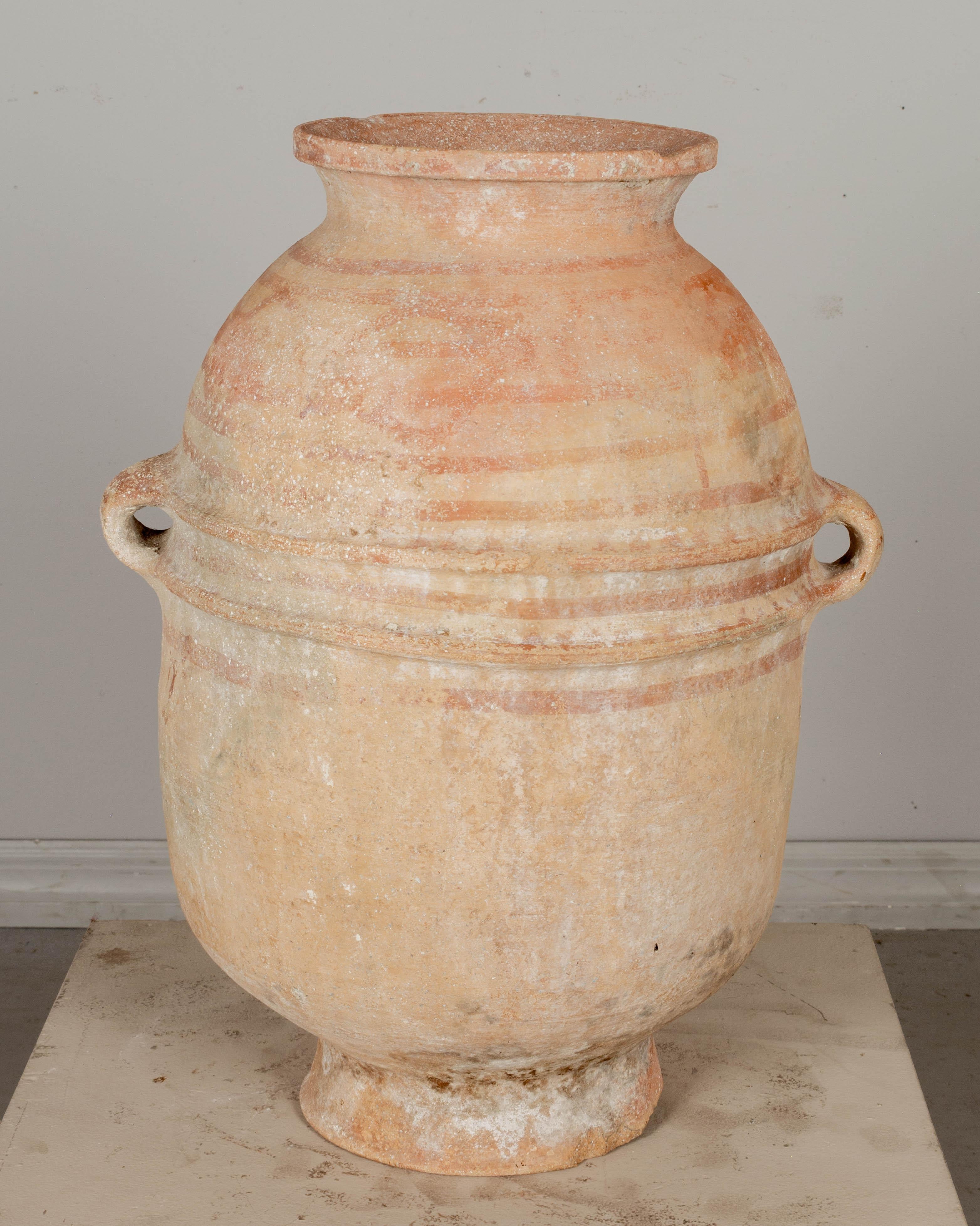 A large Moroccan terracotta pottery water jar with two small handles and faded red painted decoration. Beautiful patina. Minor chips to edge of base. 
22