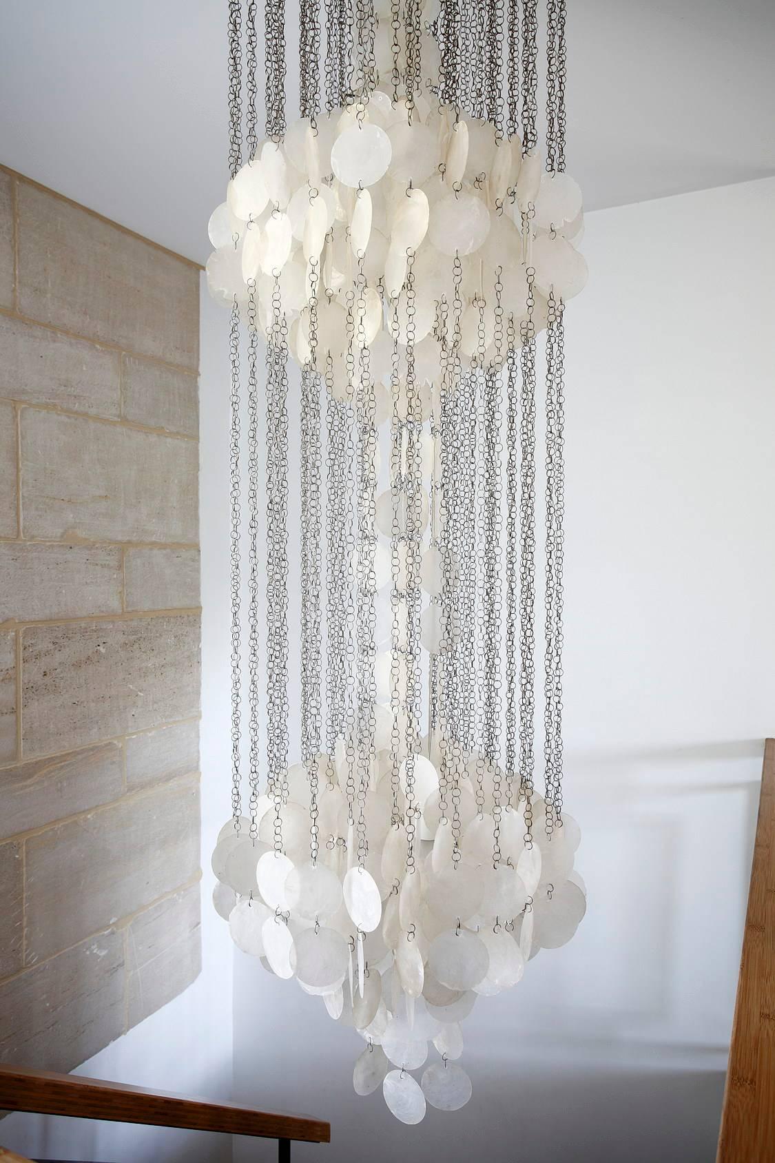 Suspended lamp composed of a white wooden round ceiling light and some metallic chains maintaining two spheres richly decorated with shells in mother of pearl. Two bulbs completely hidden by the curtains of shells create a fluid and soft light.