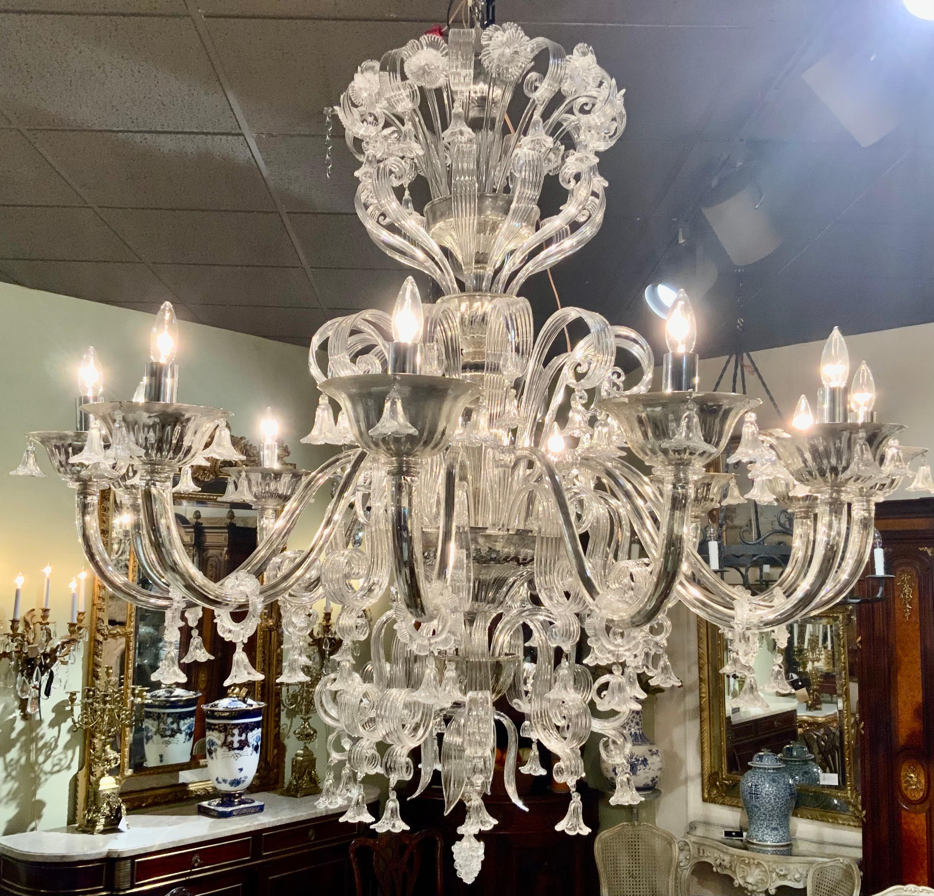 This large and dramatic chandelier has 12 scrolling glass-clad chrome arms.
With mirrored metal candle cups and a multitude of reeded scrolls, flowers.
and rings suspended with small blossoms all terminating in a delicate
floral pendant, the