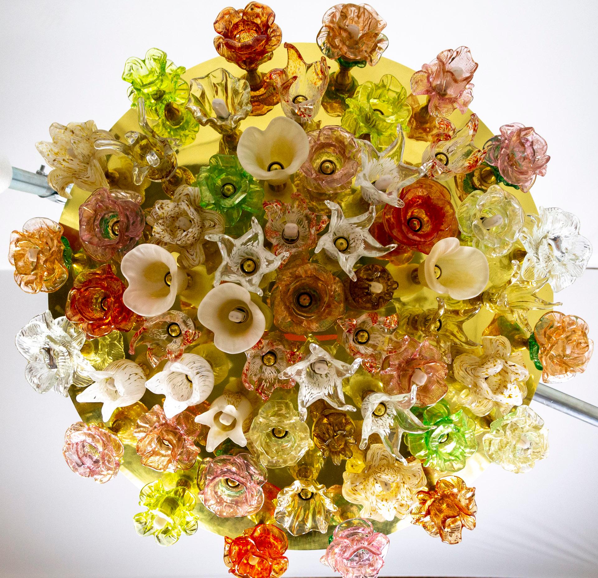 A striking, contemporary Murano design - a circular, flush mount light fixture comprised of a large, polished brass, convex disk covered with individual multi-colored, blown glass flowers. About half the flowers have sockets and illuminate with LED
