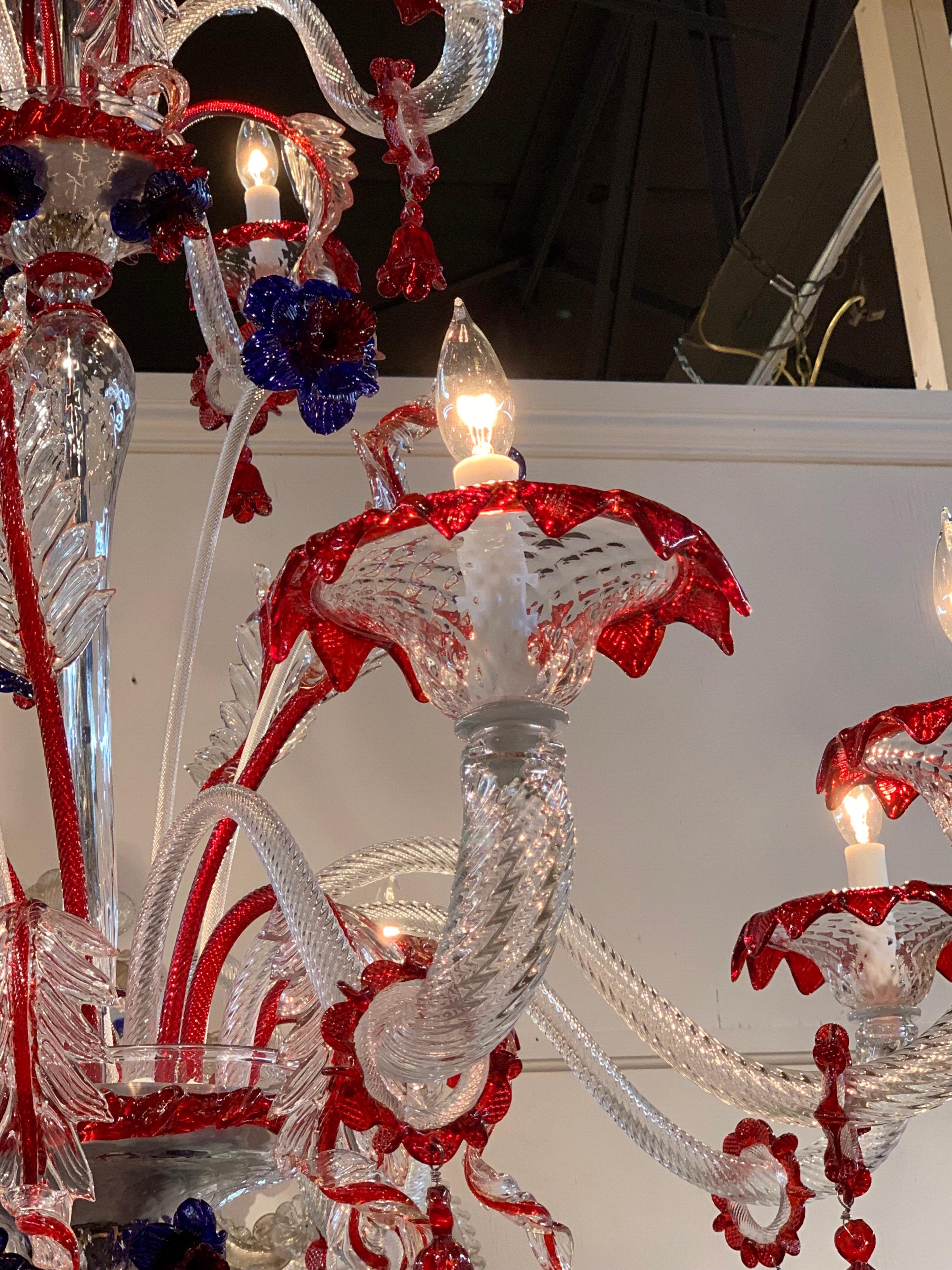 Stunning Murano glass hand blown chandelier with red and blue flowers. This fixture has 12 lights and 3 tiers of cascading flowers and leaves. This unique chandelier makes a real statement!