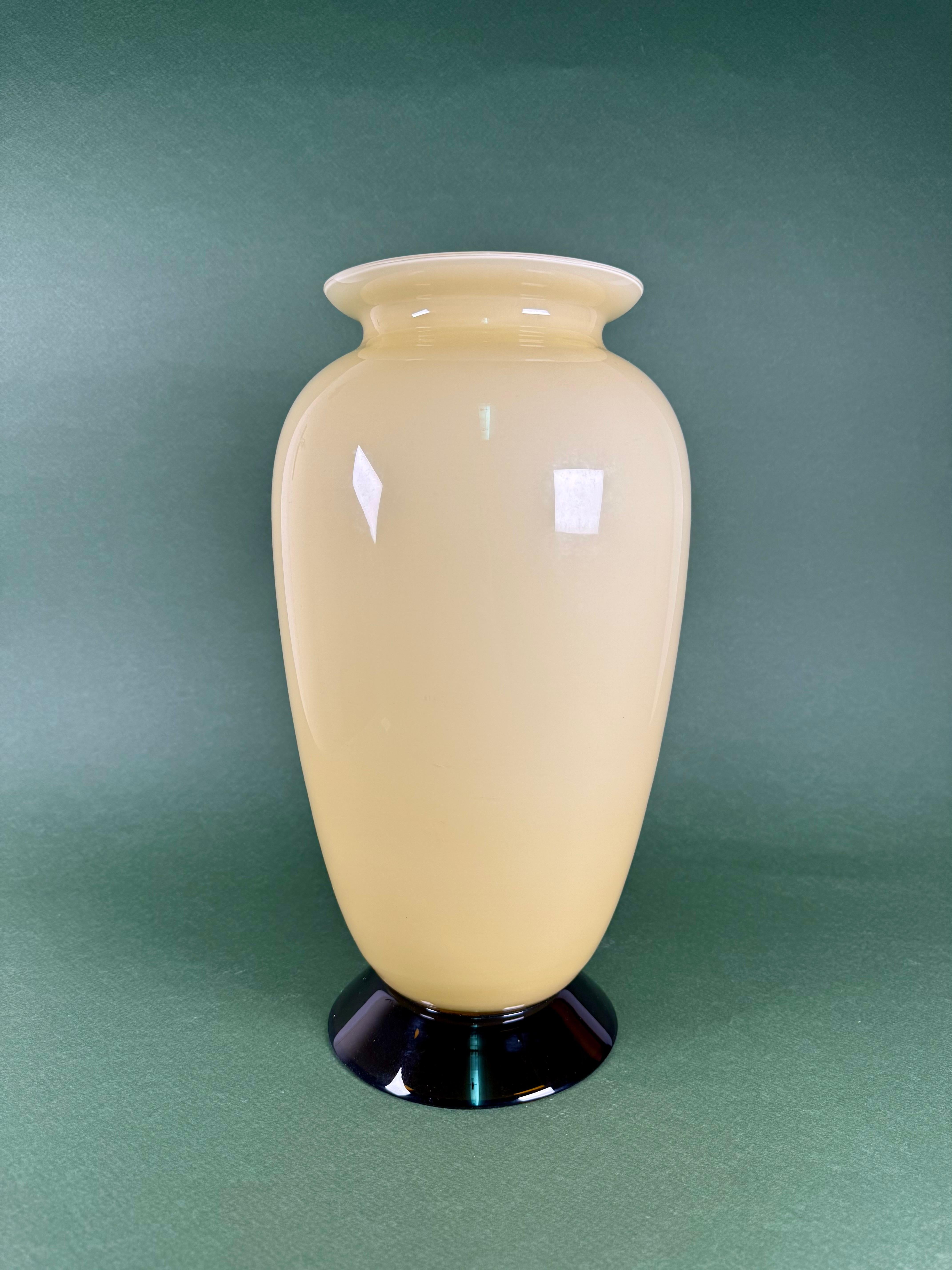 An elegant Murano glass vase from the 1980s, signed Veart Venezia, exemplifying the refined artistry of Venetian glassmaking. The vase features a luminous cream-toned body accented by a delicate yellow rim and a bold black base, creating a
