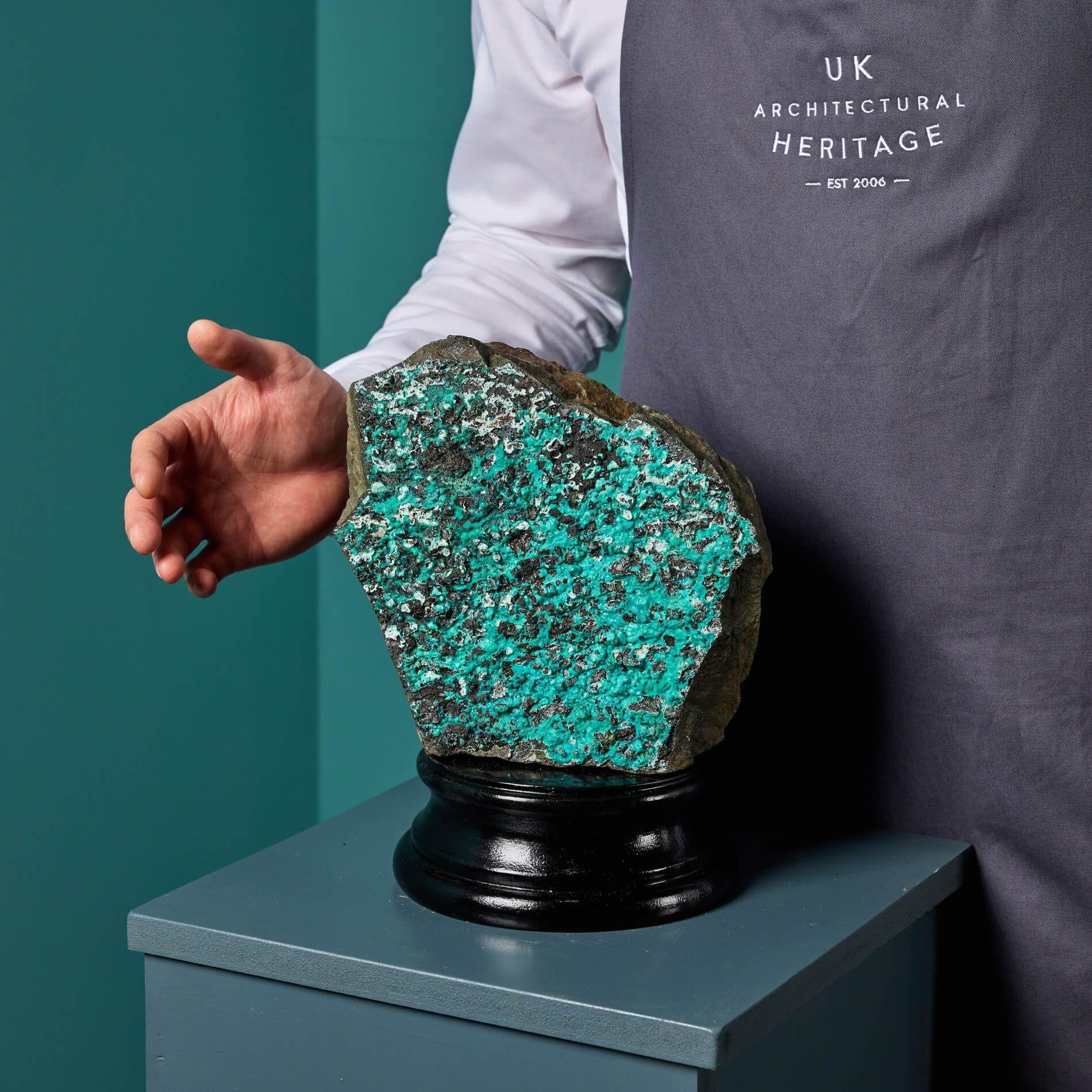 A striking large natural bedrock specimen with a coating of chrysocolla and malachite displayed on a custom neoclassical style stand.

This specimen is of an unusual irregular shape stands well showcasing its vivid colours and platelike